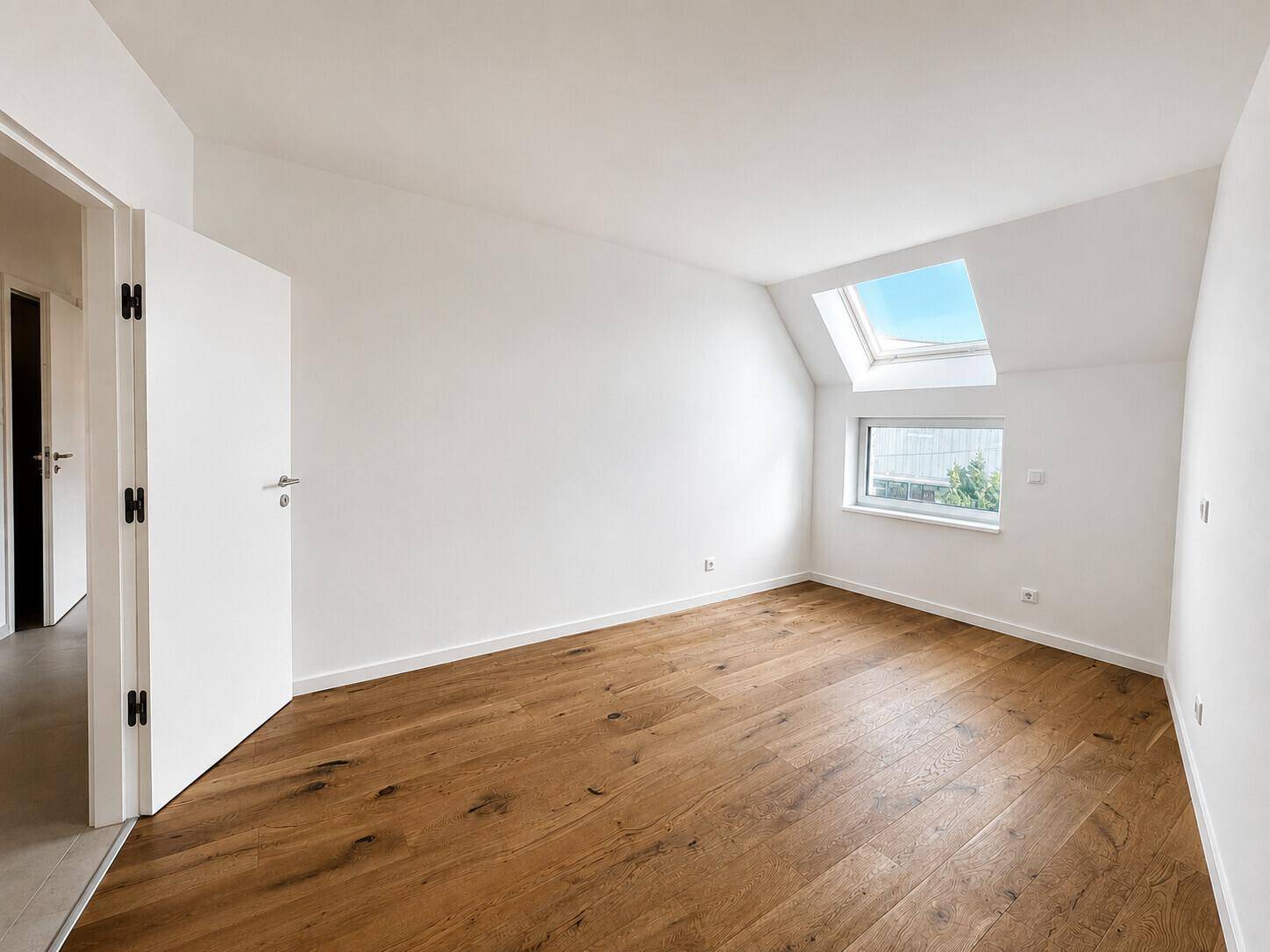 Helles Dachzimmer mit Holzboden, Dachfenster und schrägen Wänden, bietet viel natürliches Licht.