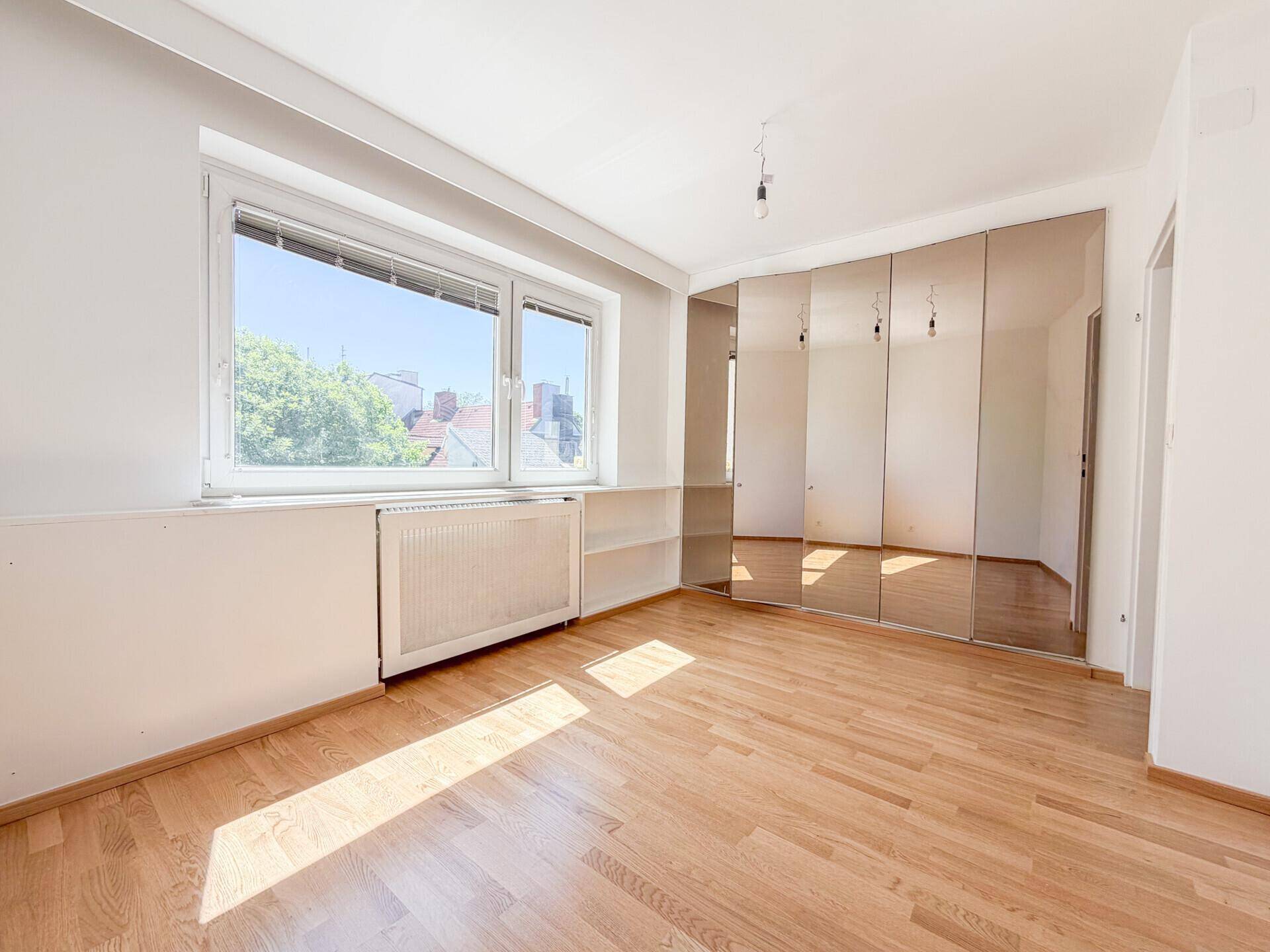 Helles Schlafzimmer mit Parkettboden und einer großen Spiegelfront, die den Raum optisch vergrößert.