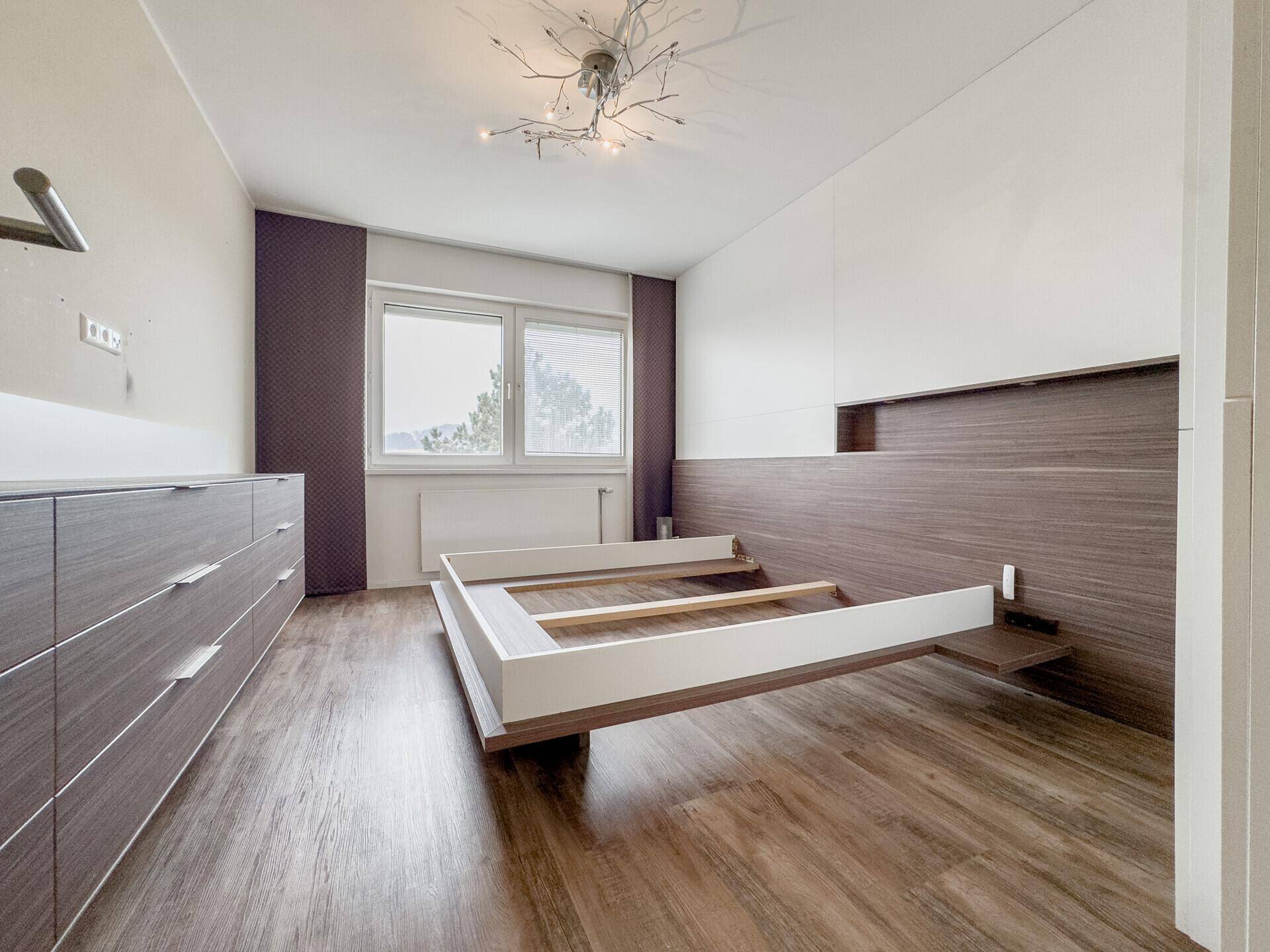 Schlafzimmer mit modernem Bettrahmen, Holzakzenten und Laminatboden, bereit zur Einrichtung.
