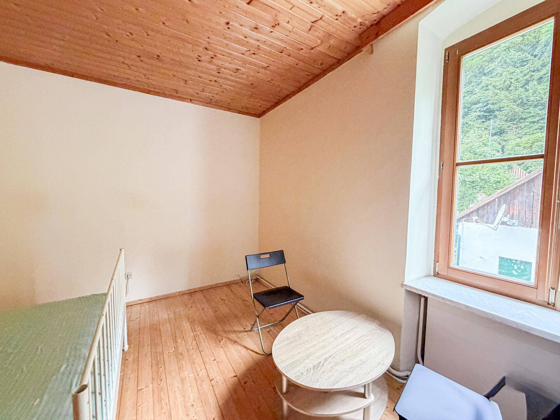 Einfaches Schlafzimmer mit Holzdielenboden, Holzdecke und Blick ins Grüne.