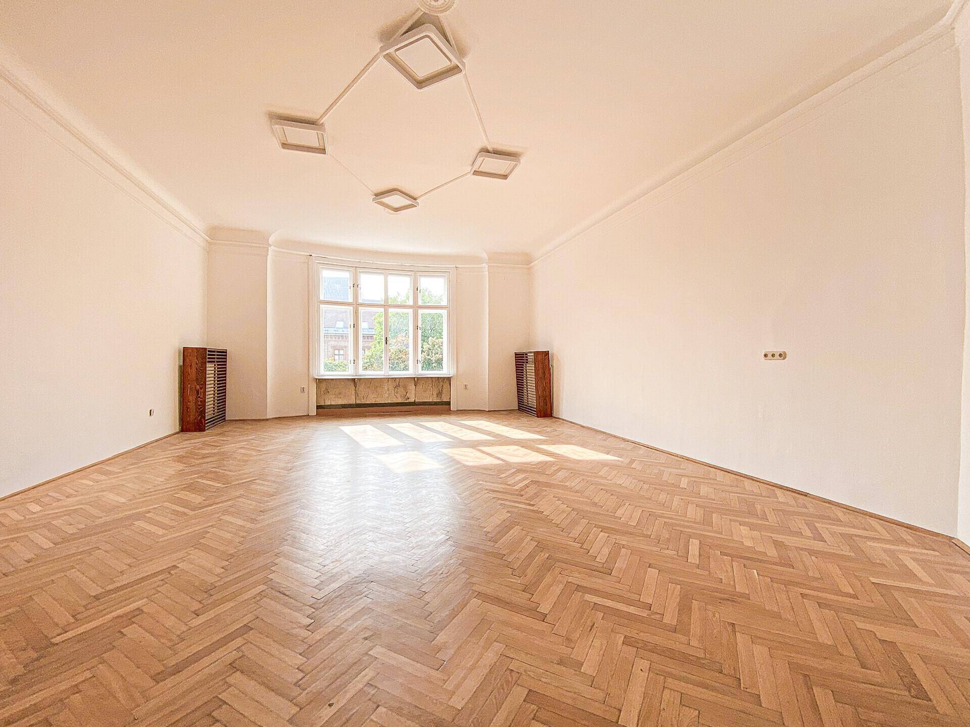 Geräumiges, helles Zimmer mit Fischgrätparkett und hohen Decken, ideal für Wohn- oder Arbeitsbereich.