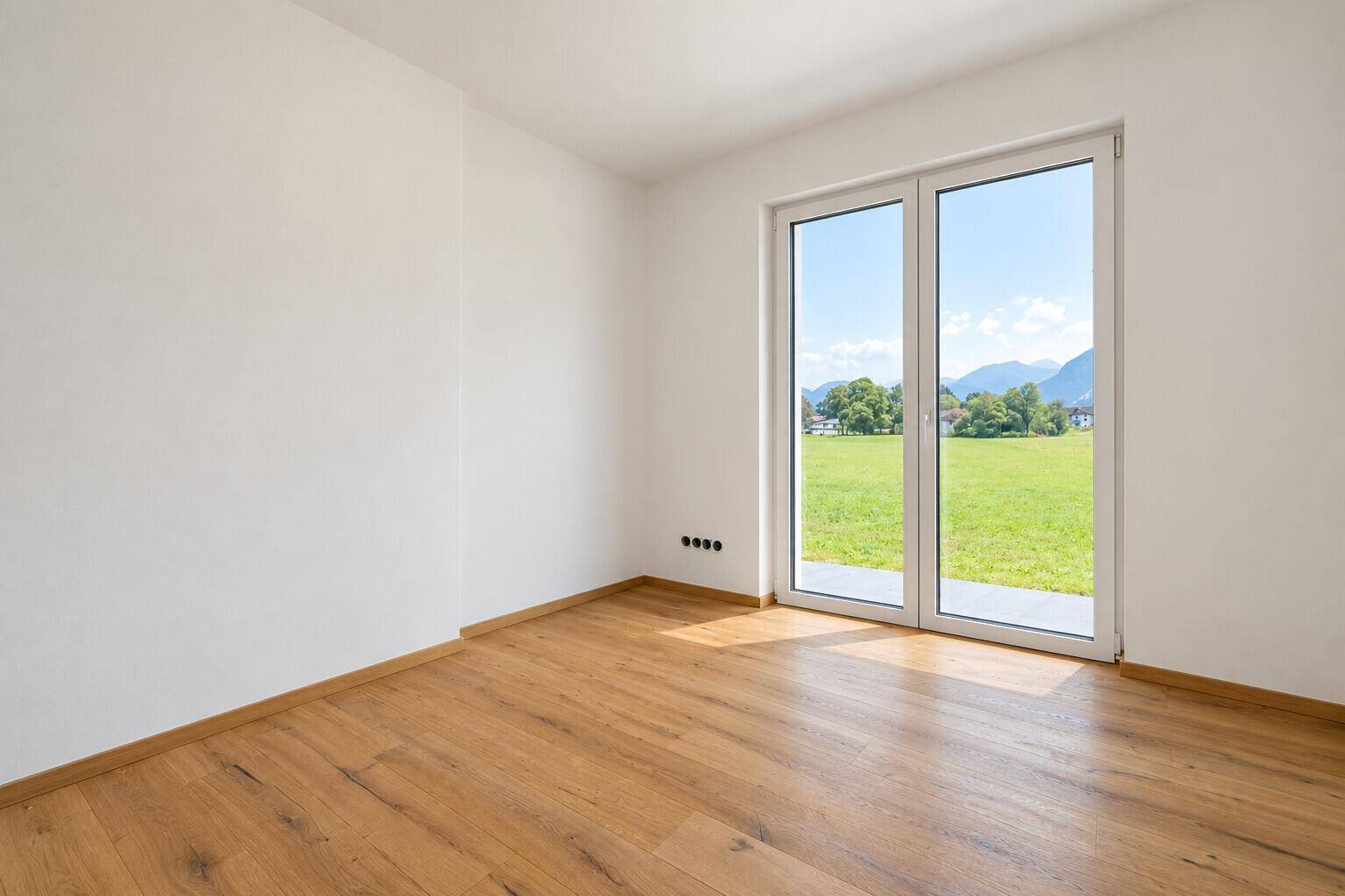 Lichtdurchfluteter Raum mit Holzboden und großen Fenstern mit Blick ins Grüne.