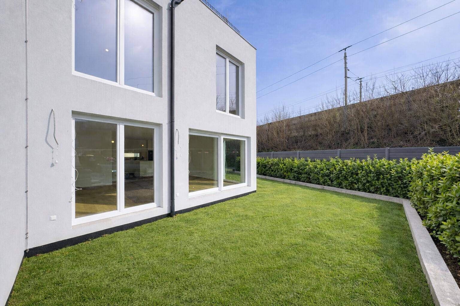 Moderne Gebäudefassade mit großen Fenstern und einem gepflegten Rasenbereich mit Hecke.
