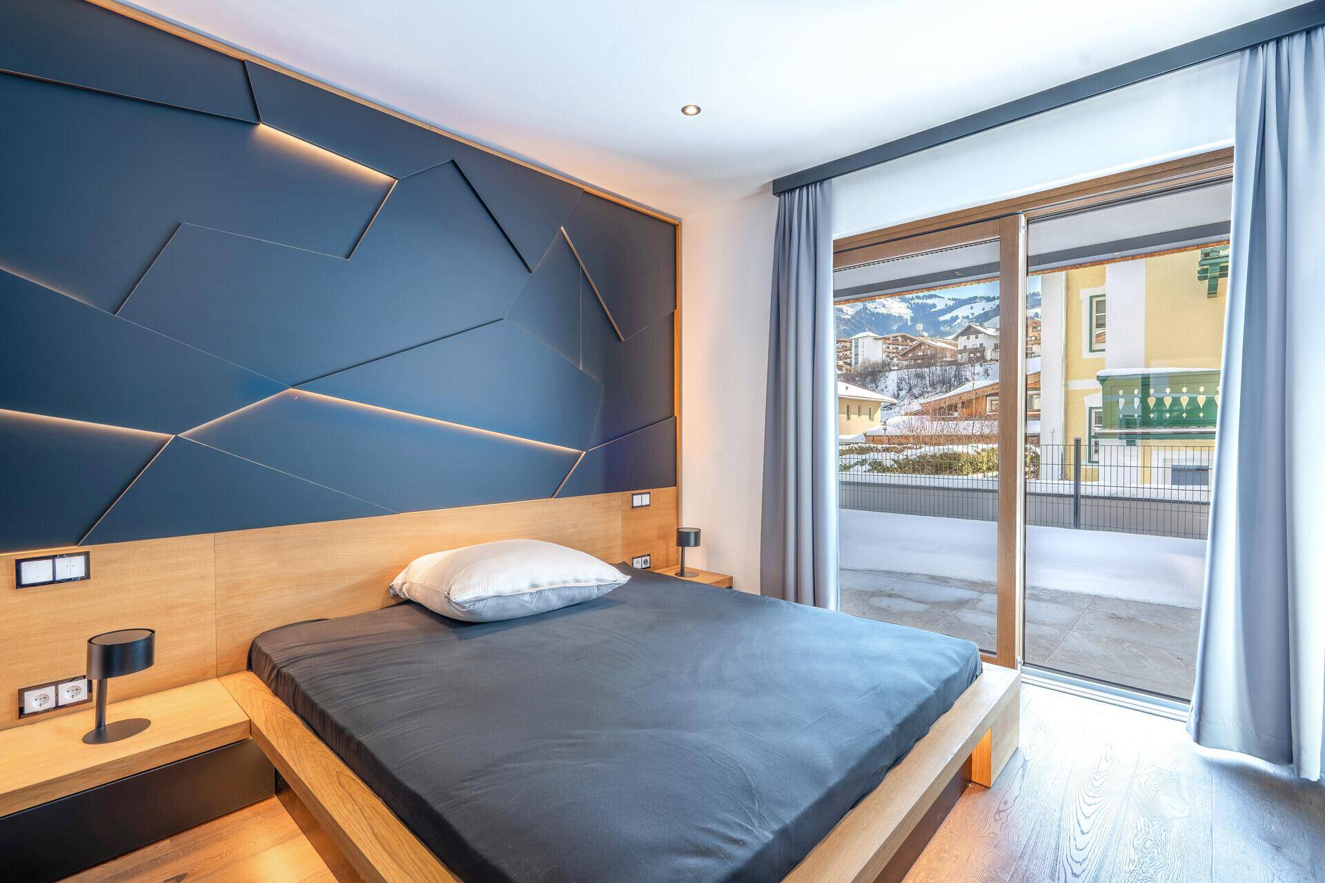 Helles Schlafzimmer mit Holzbett, moderner Wandgestaltung und Bergblick durch die Terrassentür.