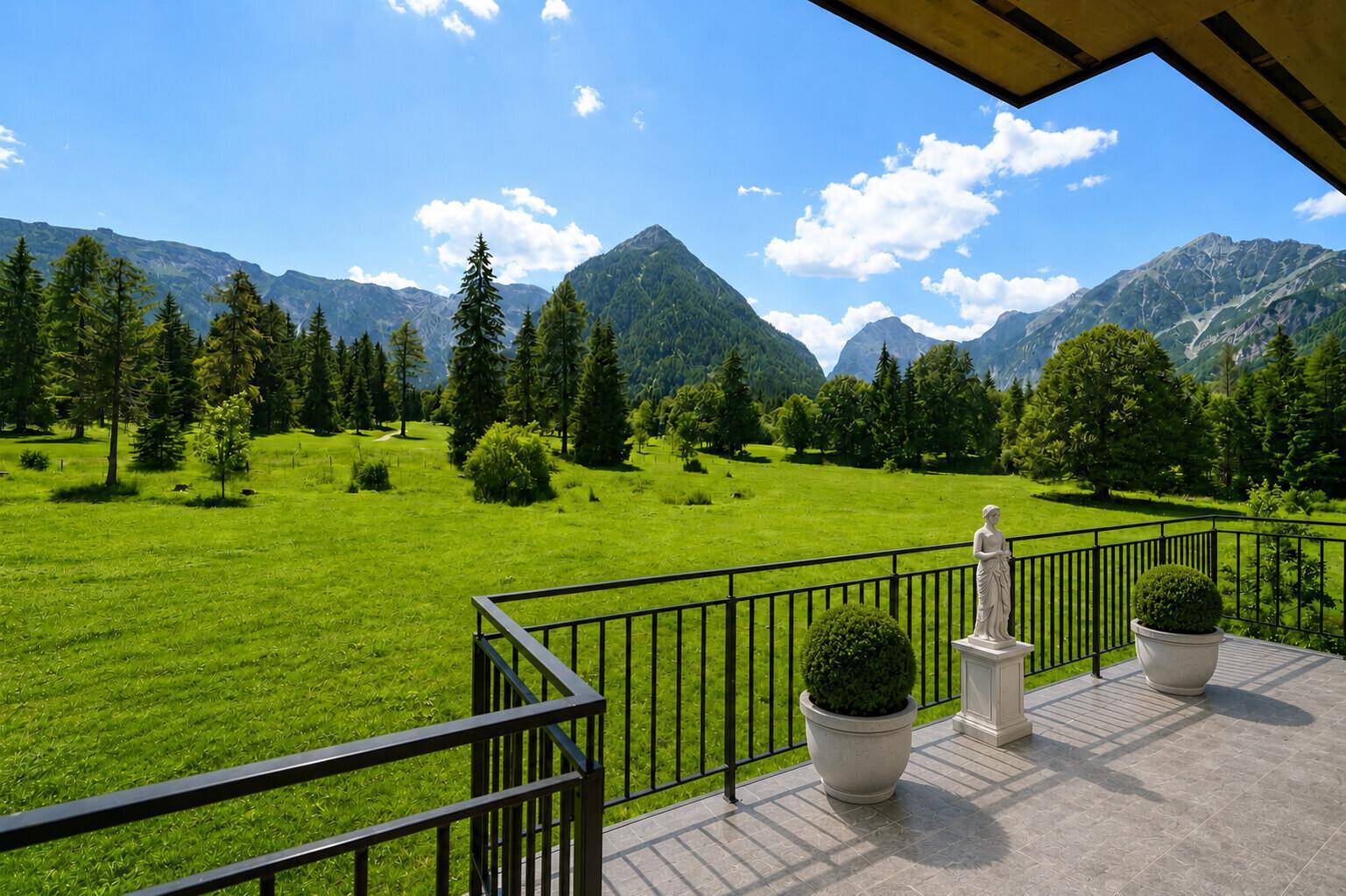 Sonnige Terrasse mit Panoramablick auf grüne Wiesen und majestätische Berge unter blauem Himmel.