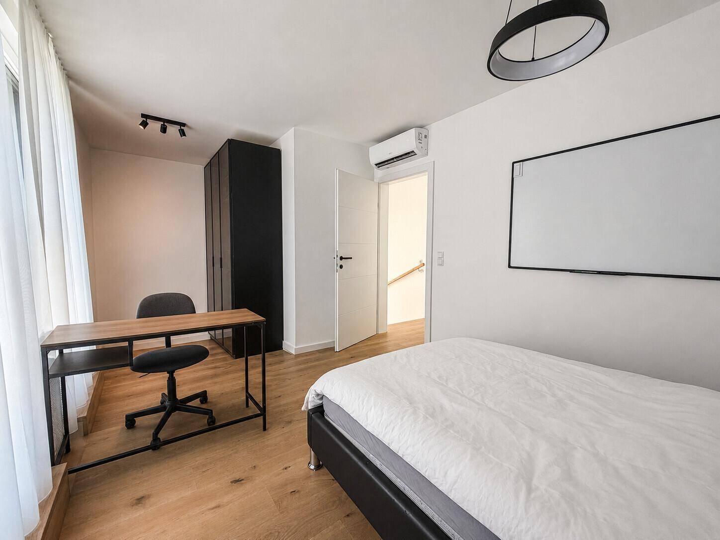 Helles Zimmer mit Schreibtisch, Kleiderschrank, Klimaanlage und Holzboden.