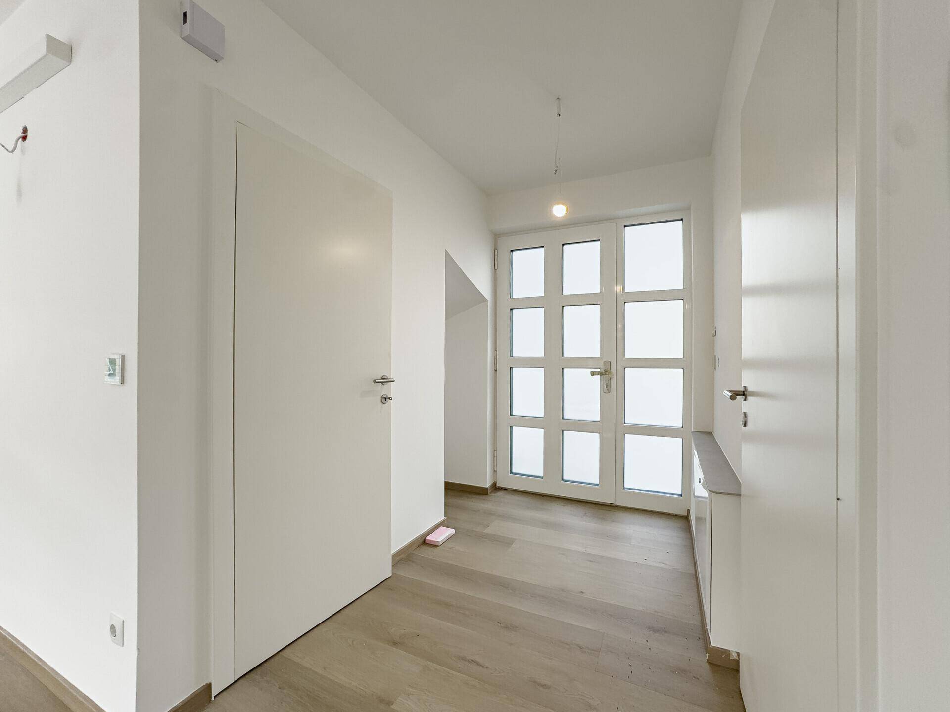 Heller Eingangsbereich mit moderner Haustür und Holzboden, der in die Wohnräume führt.