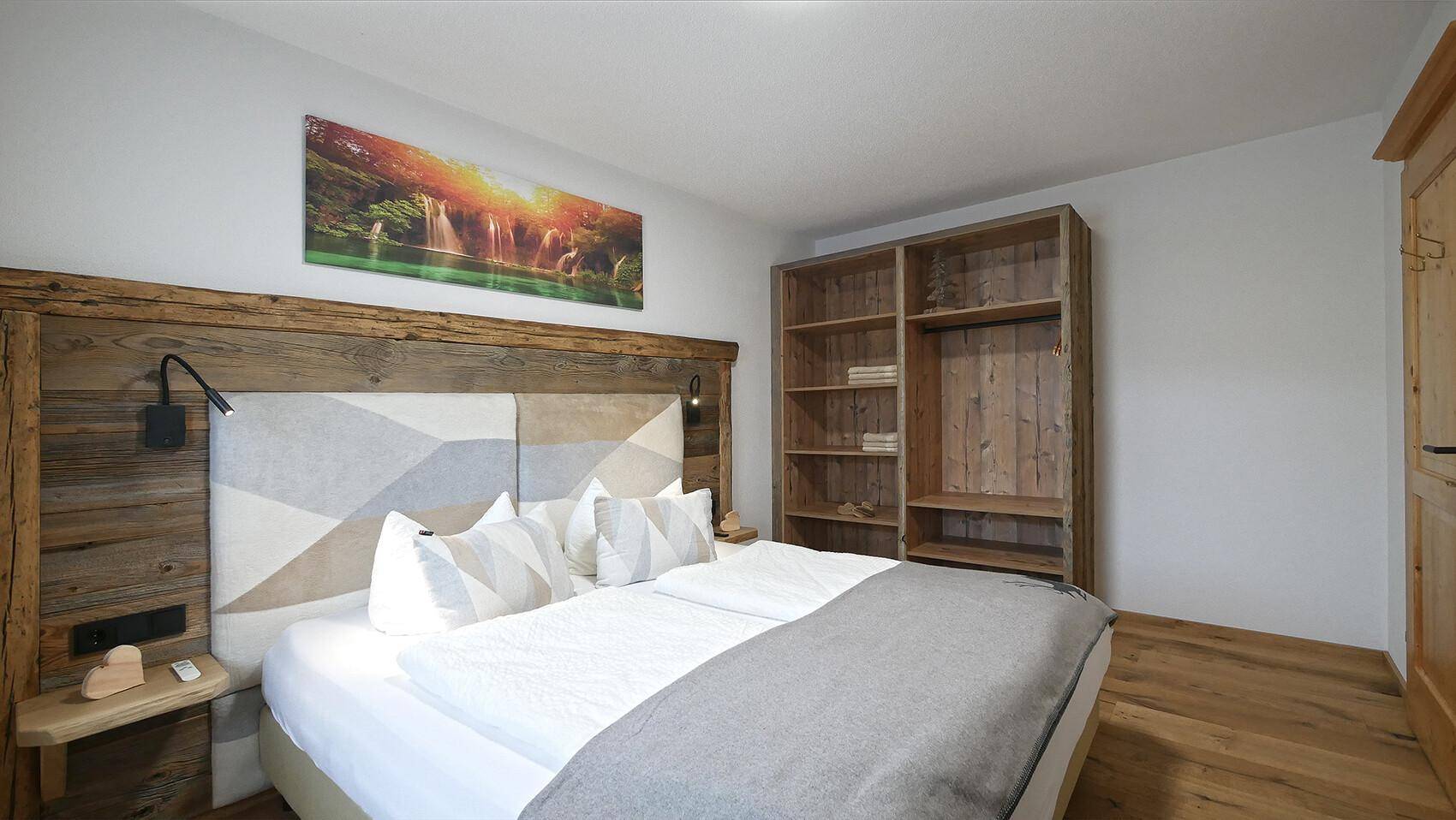 Schlafzimmer mit rustikalem Holzbett, offenem Kleiderschrank und Holzboden.