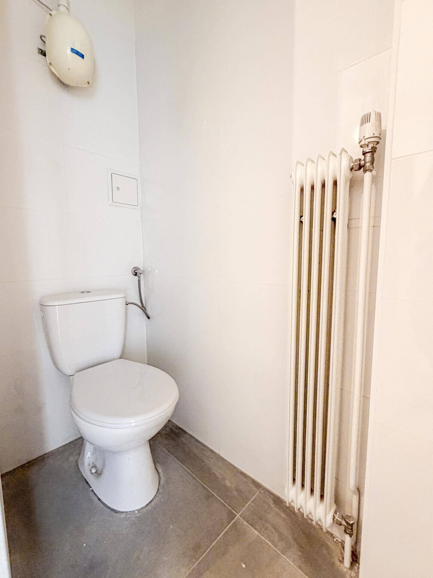 Separates WC mit Toilette, Heizkörper und hellen Fliesen an Wänden und Boden.