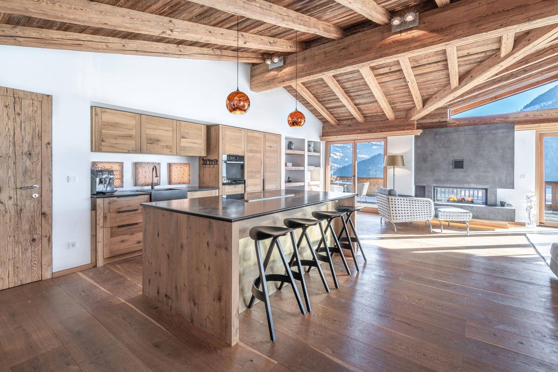 Moderne Holzküche mit Kücheninsel, integrierten Geräten und Blick auf den Wohnbereich mit Kamin.
