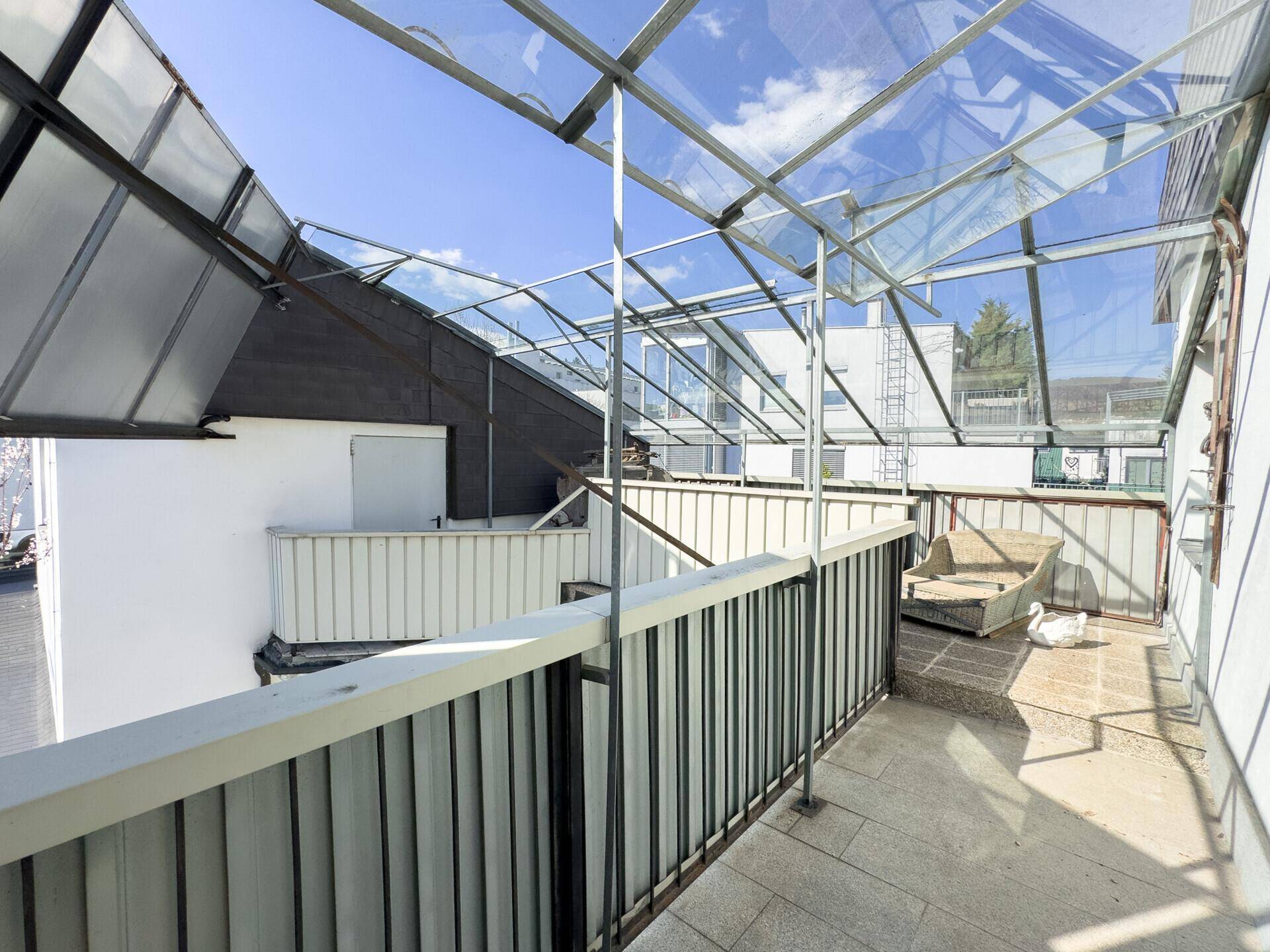 Überdachter Balkon mit Glasdachkonstruktion und Fliesenboden, bietet Schutz und Ausblick.