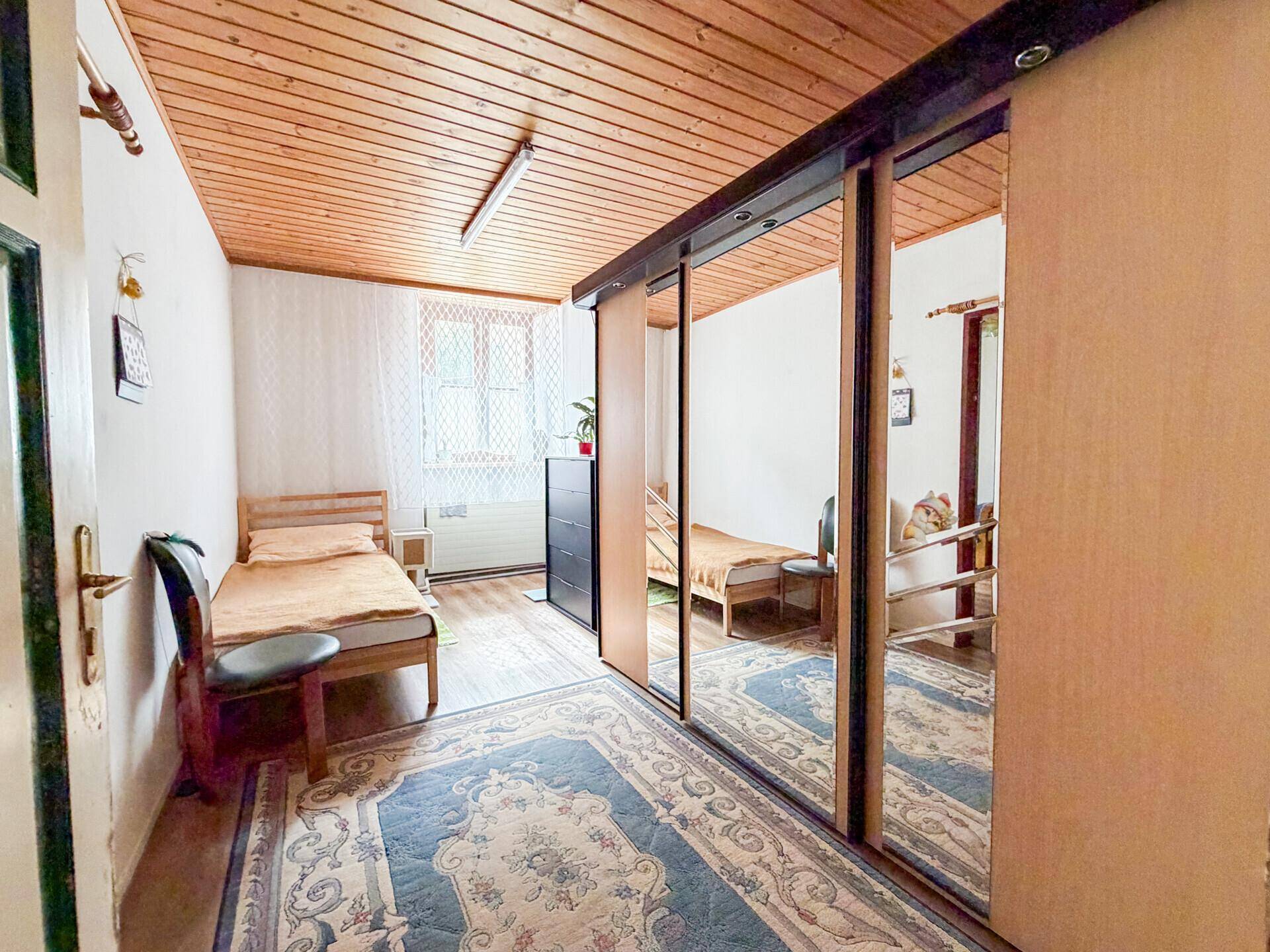 Schlafzimmer mit Holzdielenboden, Holzdecke und einem großen Spiegelschrank.
