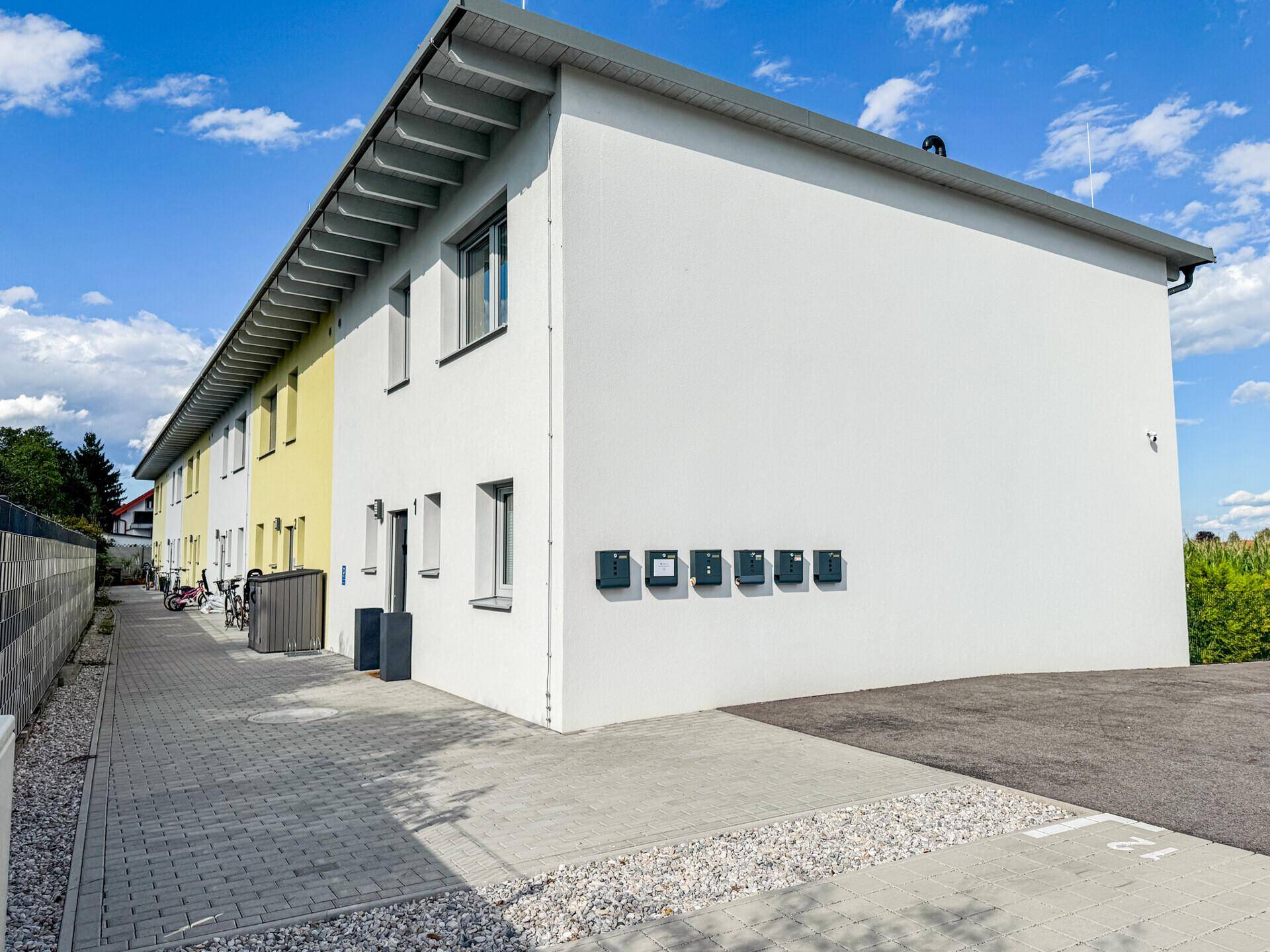 Moderne Reihenhäuser mit weißer Fassade, Briefkästen und gepflastertem Zugangsbereich.