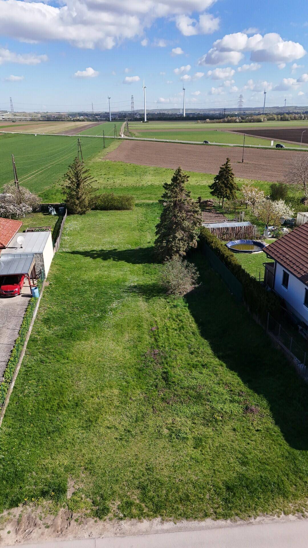 Luftaufnahme des Grundstücks mit angrenzenden Feldern und Windrädern am Horizont.