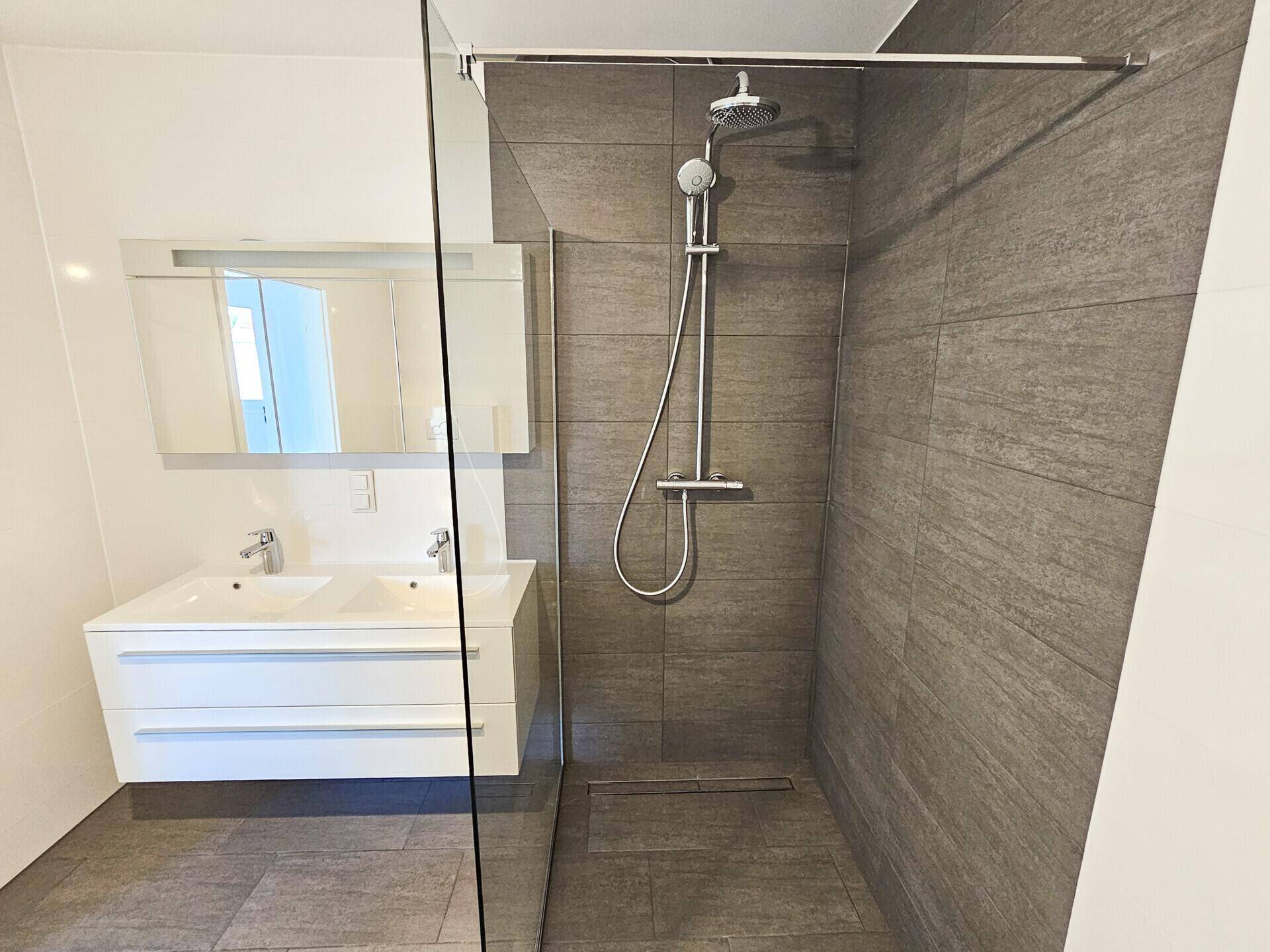 Großzügige begehbare Dusche mit Regenduschkopf und Doppelwaschbecken im modernen Bad.