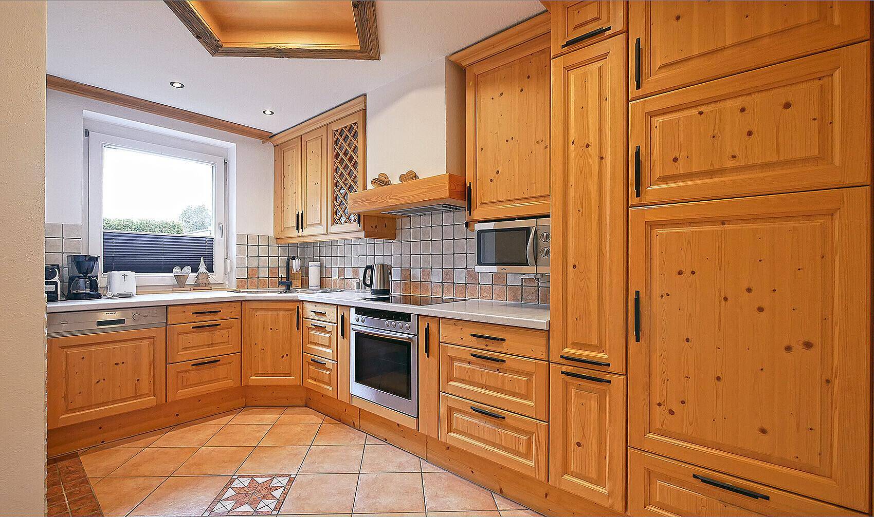 Traditionelle Holzküche mit Einbaugeräten, Fliesenboden und Fenster.