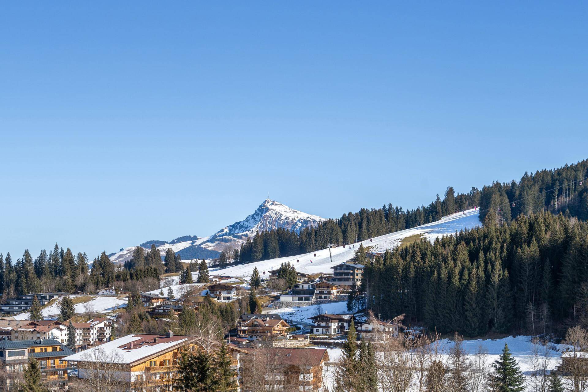 Panoramablick auf die verschneite Berglandschaft mit umliegenden Häusern und Skipisten.