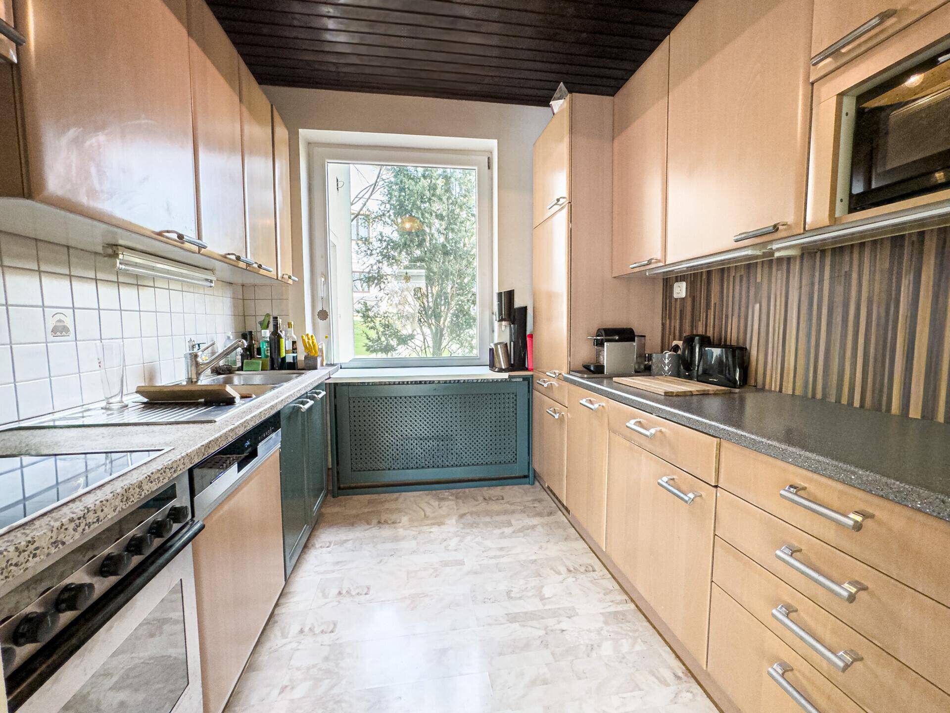 Funktionale Küche mit Holzschränken, Granitarbeitsplatte und Fenster mit Blick ins Grüne.