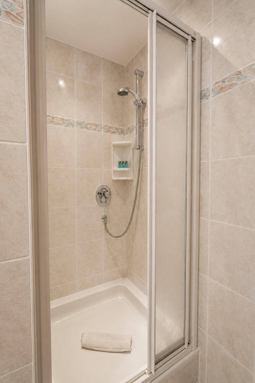 Duschbereich im Badezimmer mit beigefarbenen Fliesen und Glastür für eine moderne Optik.