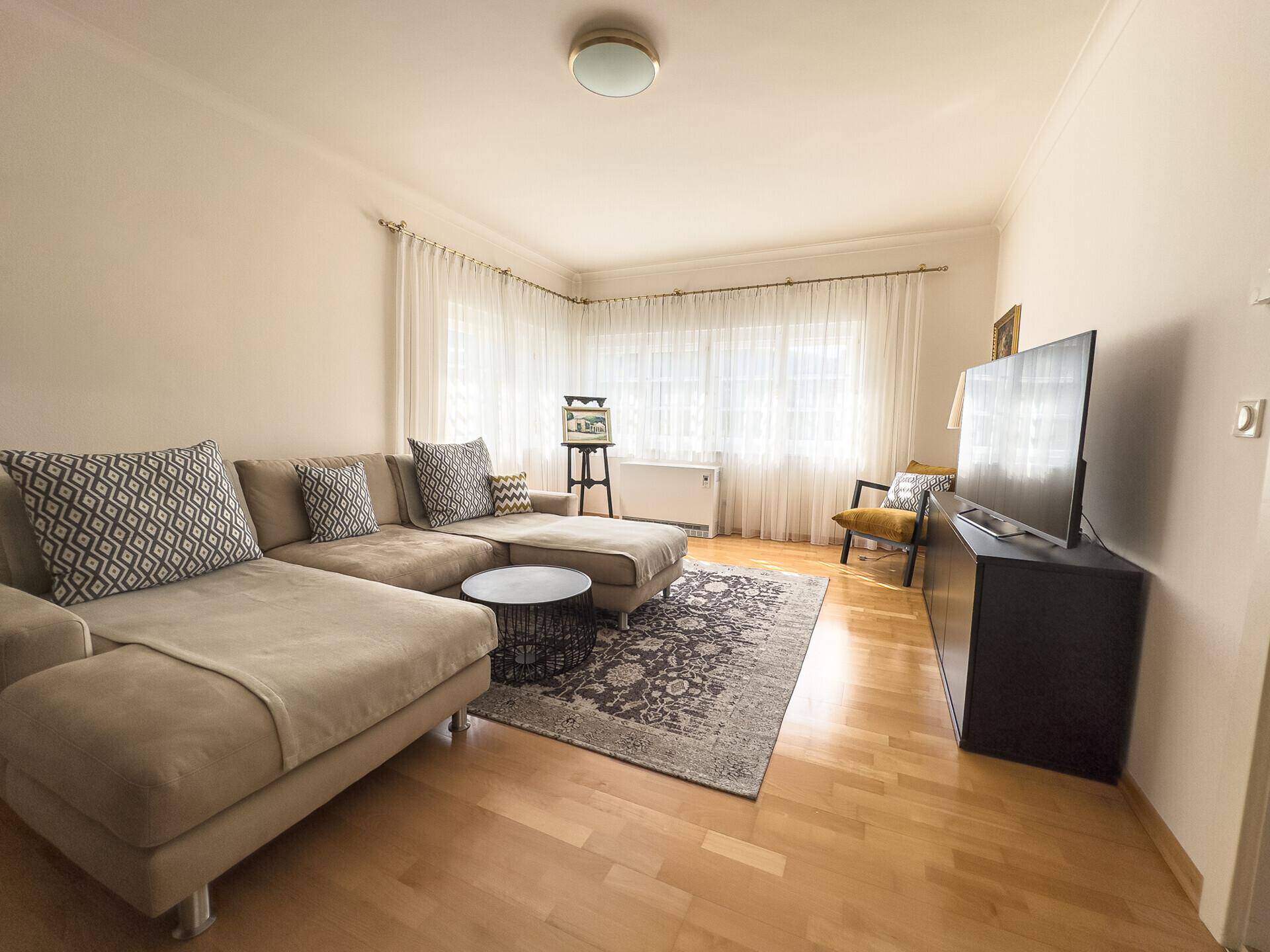 Gemütliches Wohnzimmer mit Sofa, Holzboden und großen Fenstern.