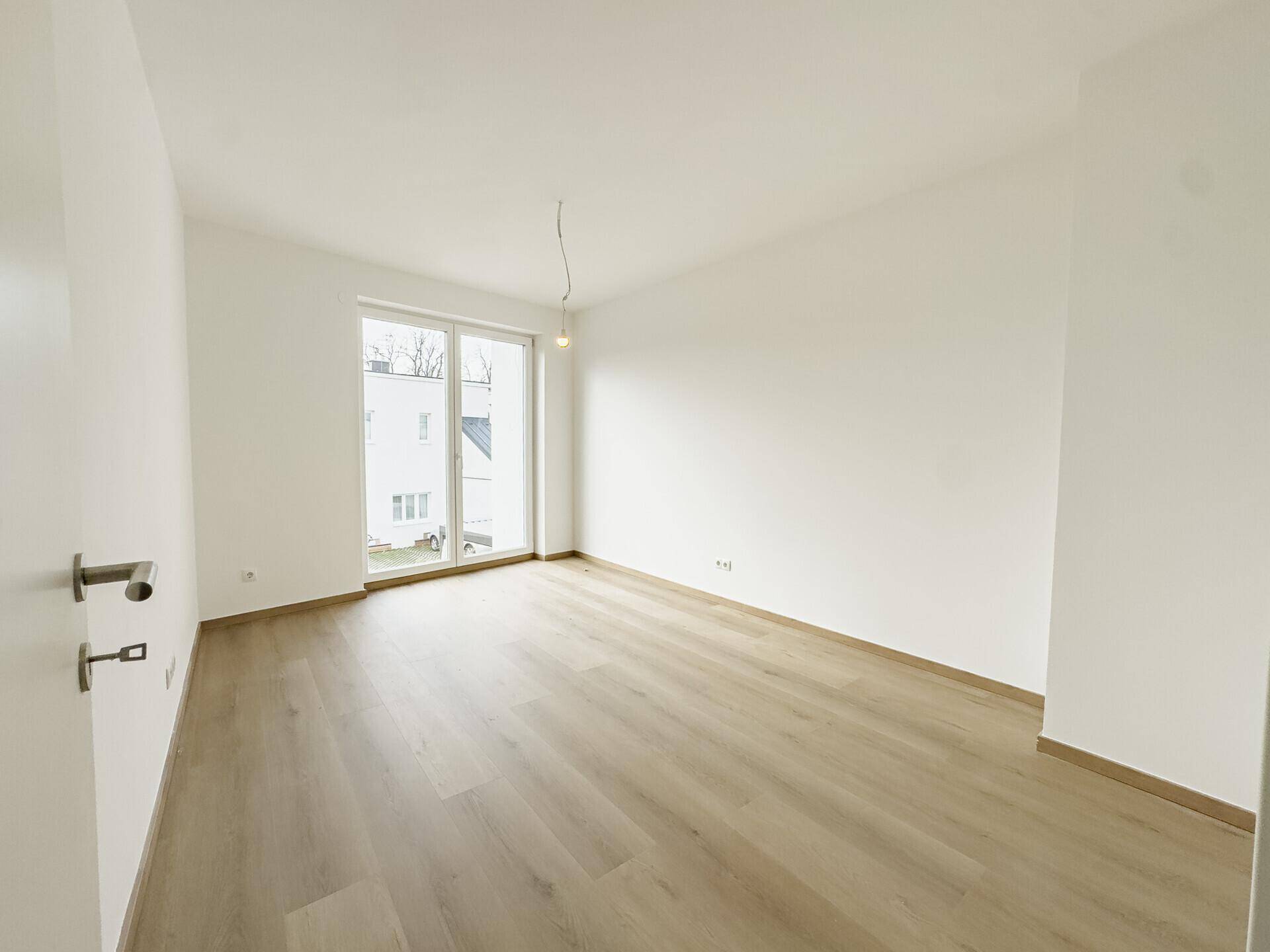 Helles Schlafzimmer mit Holzboden und großem Fenster, das einen Blick nach draußen ermöglicht.