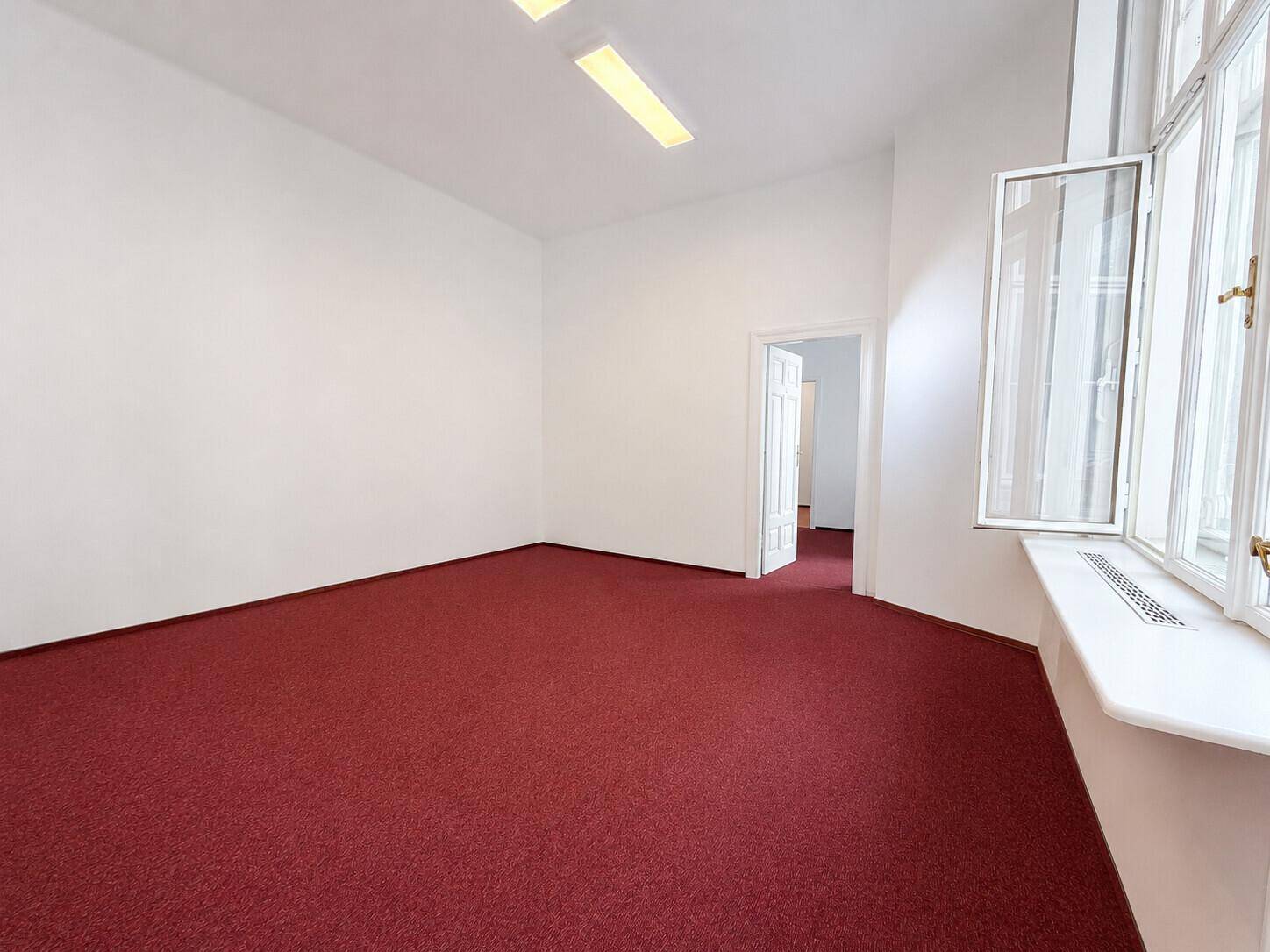 Helles Zimmer mit rotem Teppichboden und großem Fenster, das viel Tageslicht bietet.