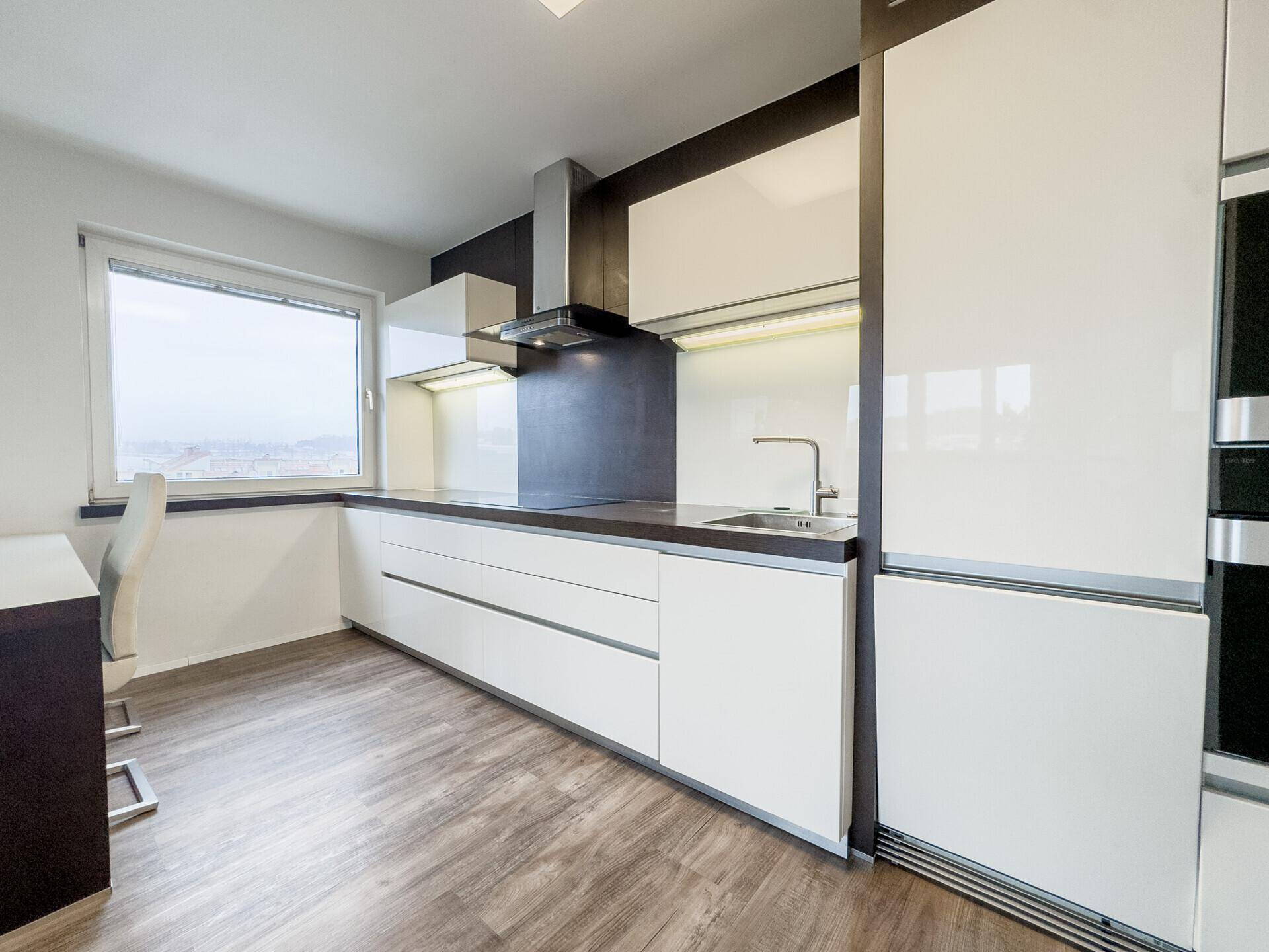 Stilvolle weiße Küche mit dunkler Arbeitsplatte, Spüle und integriertem Kochfeld unter Dunstabzugshaube.