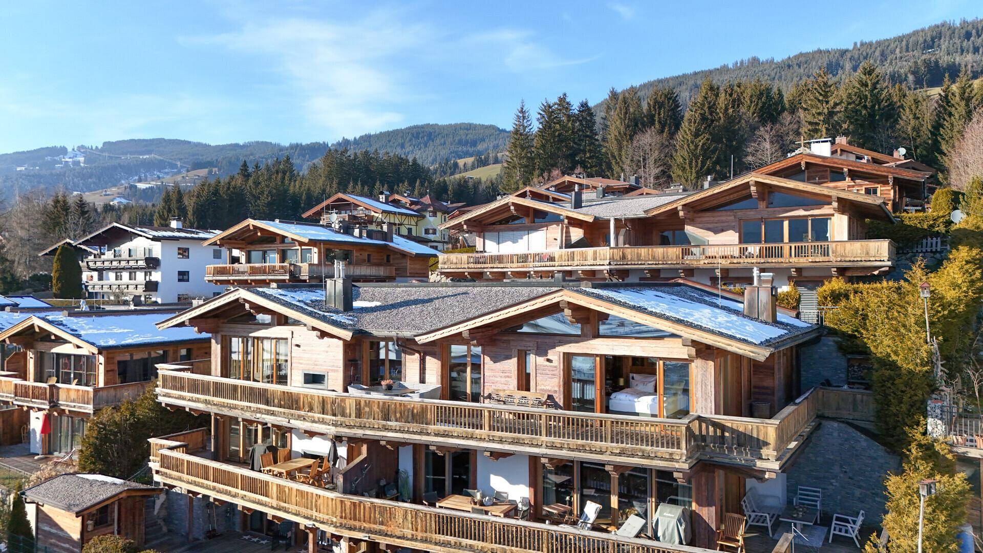 Panoramablick auf luxuriöse Holzchalets mit großzügigen Balkonen und Terrassen, eingebettet in eine alpine Berglandschaft.