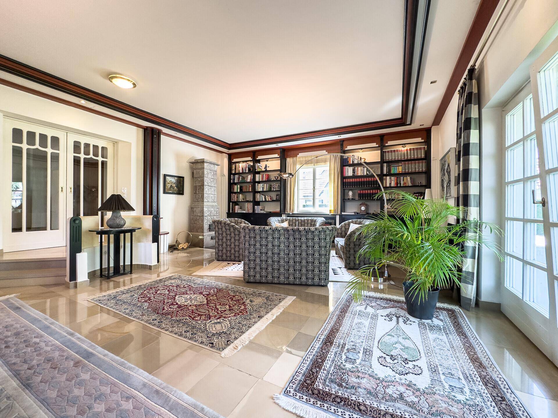 Großzügiges Wohnzimmer mit Bücherregalen, Sitzgelegenheiten und Zugang zum Garten.