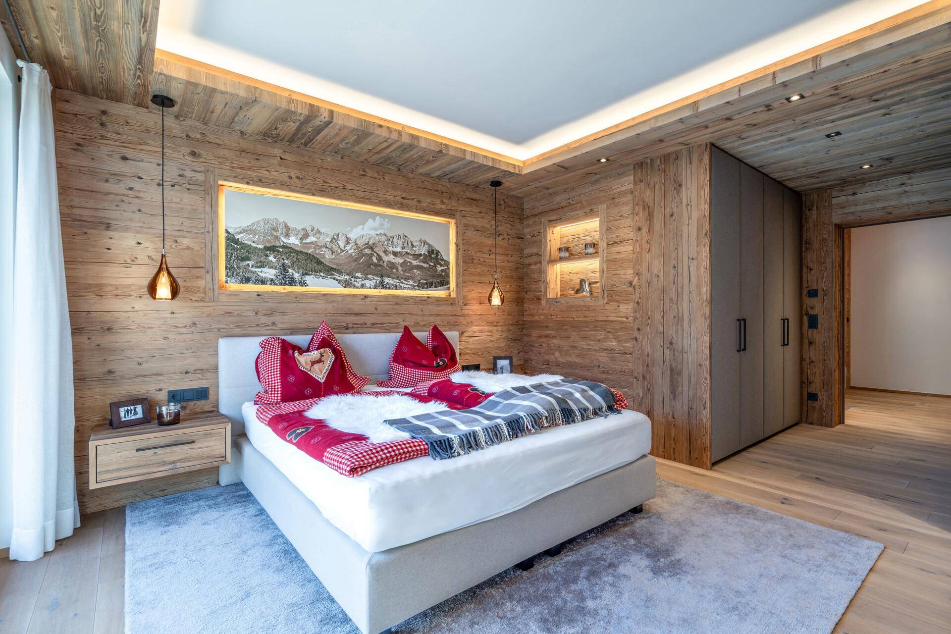 Gemütliches Schlafzimmer im alpinen Stil mit Holzwänden, indirekter Beleuchtung und großem Bett.