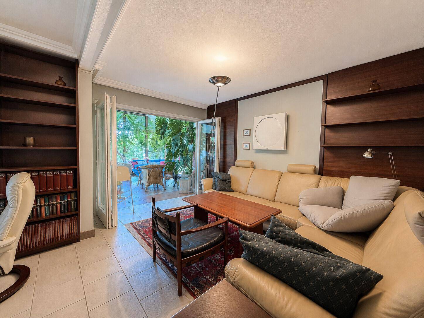 Wohnzimmer mit beigem Ledersofa, Bücherregalen und direktem Zugang zum Wintergarten.