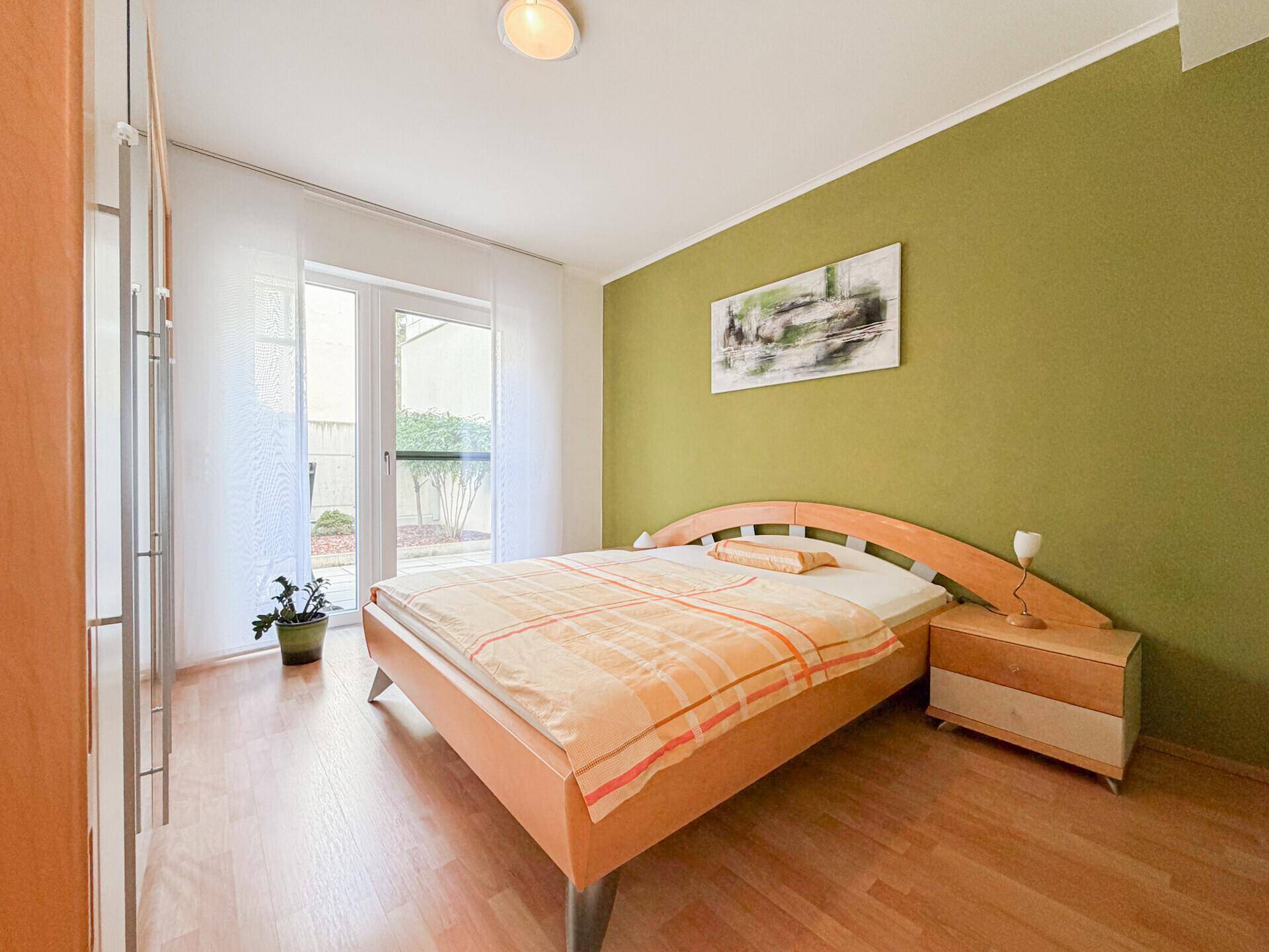 Schlafzimmer mit Holzbett, grün gestrichener Wand und Zugang zu einem Außenbereich.