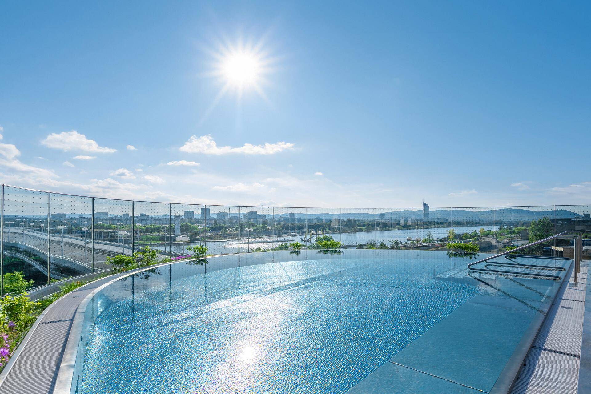Atemberaubender Infinity-Pool auf dem Dach mit Panoramablick über die Stadt und den Fluss unter strahlendem Sonnenschein.