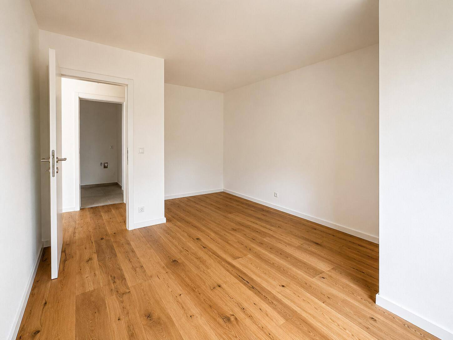 Leeres Schlafzimmer mit Holzboden und weiß gestrichenen Wänden, bereit zur Einrichtung.