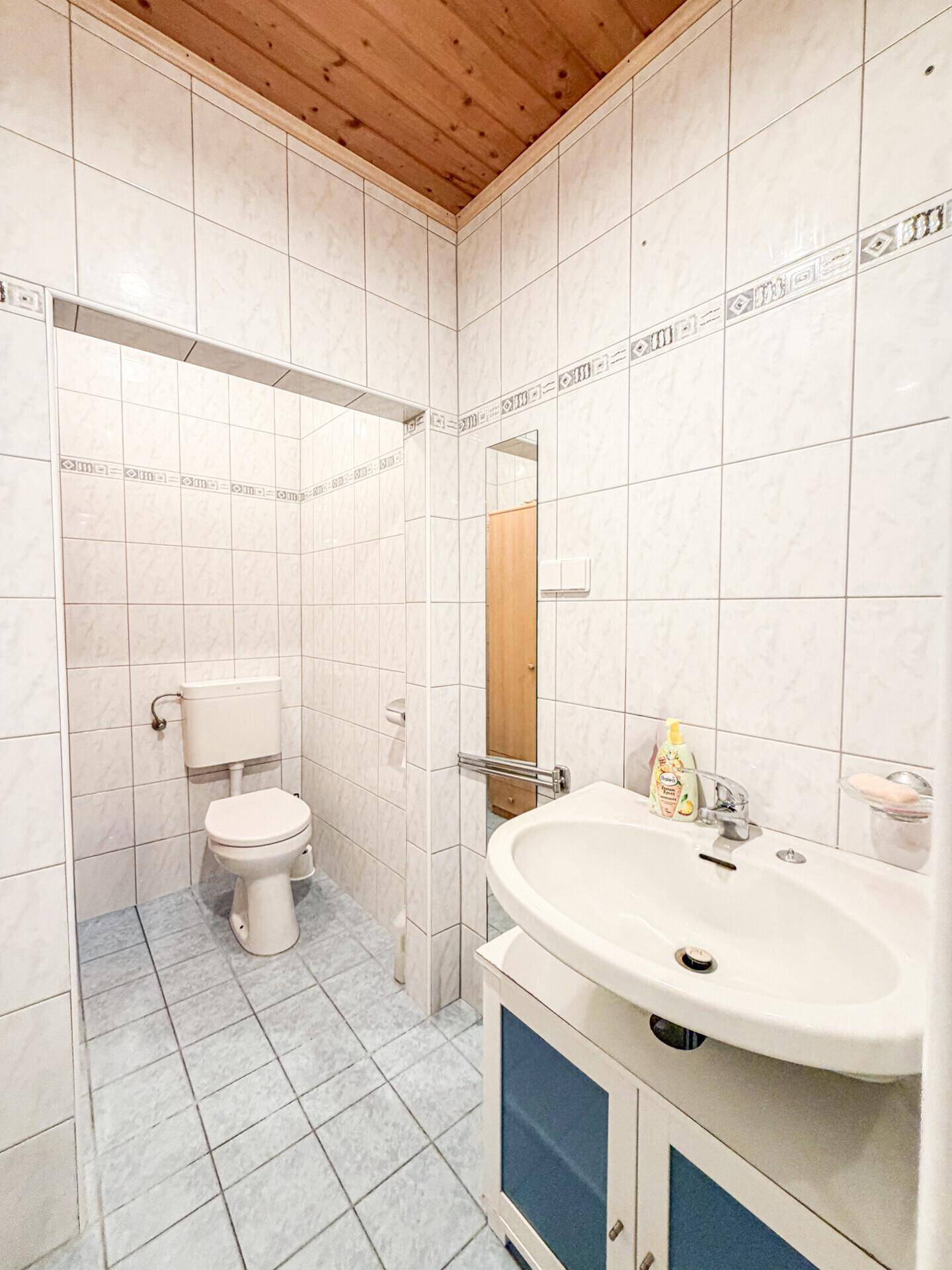 Badezimmer mit WC, Waschbecken und weißen Fliesen.