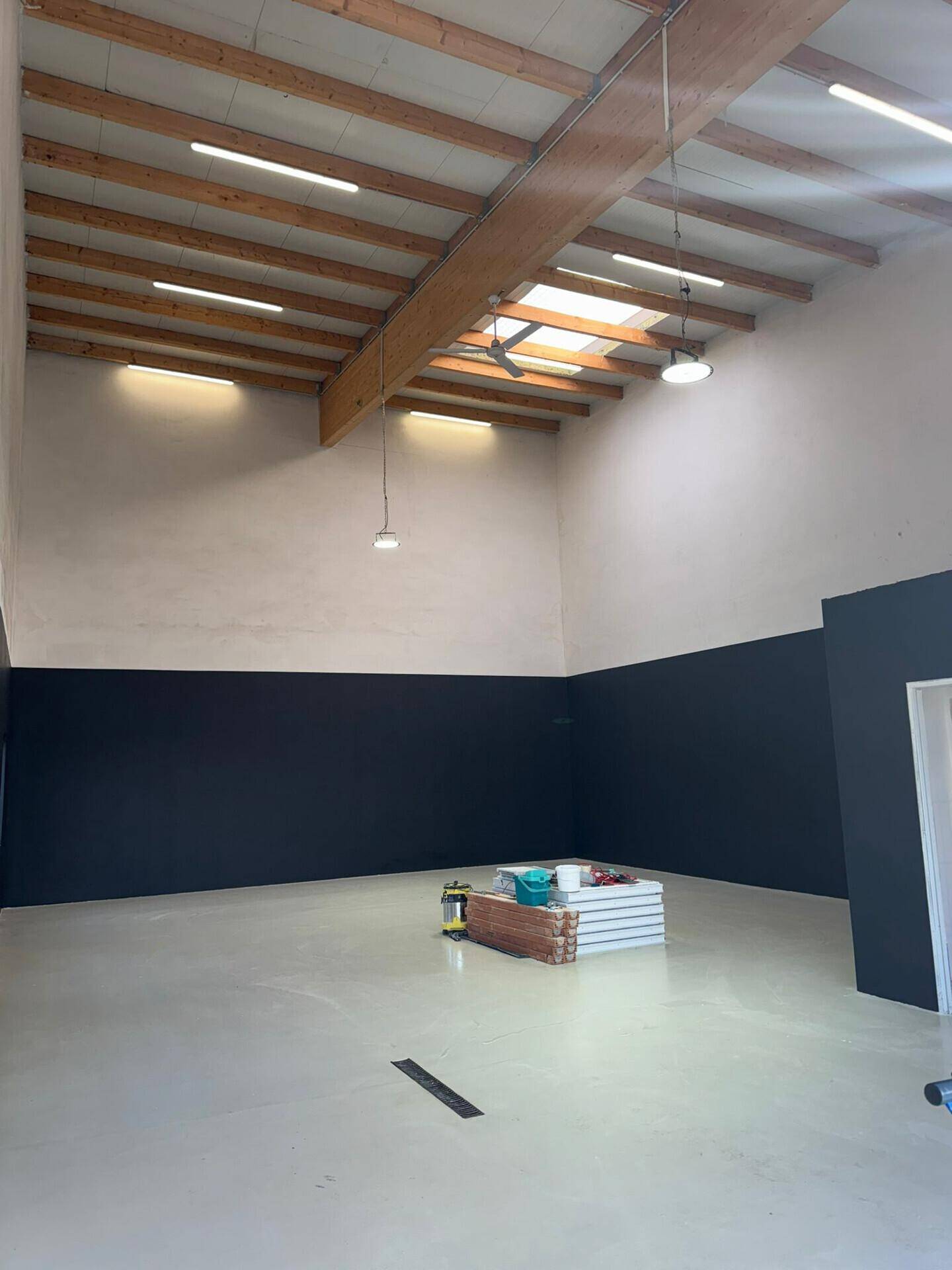 Innenansicht einer geräumigen Garage mit hohen Decken, sichtbaren Holzbalken und Deckenventilatoren.