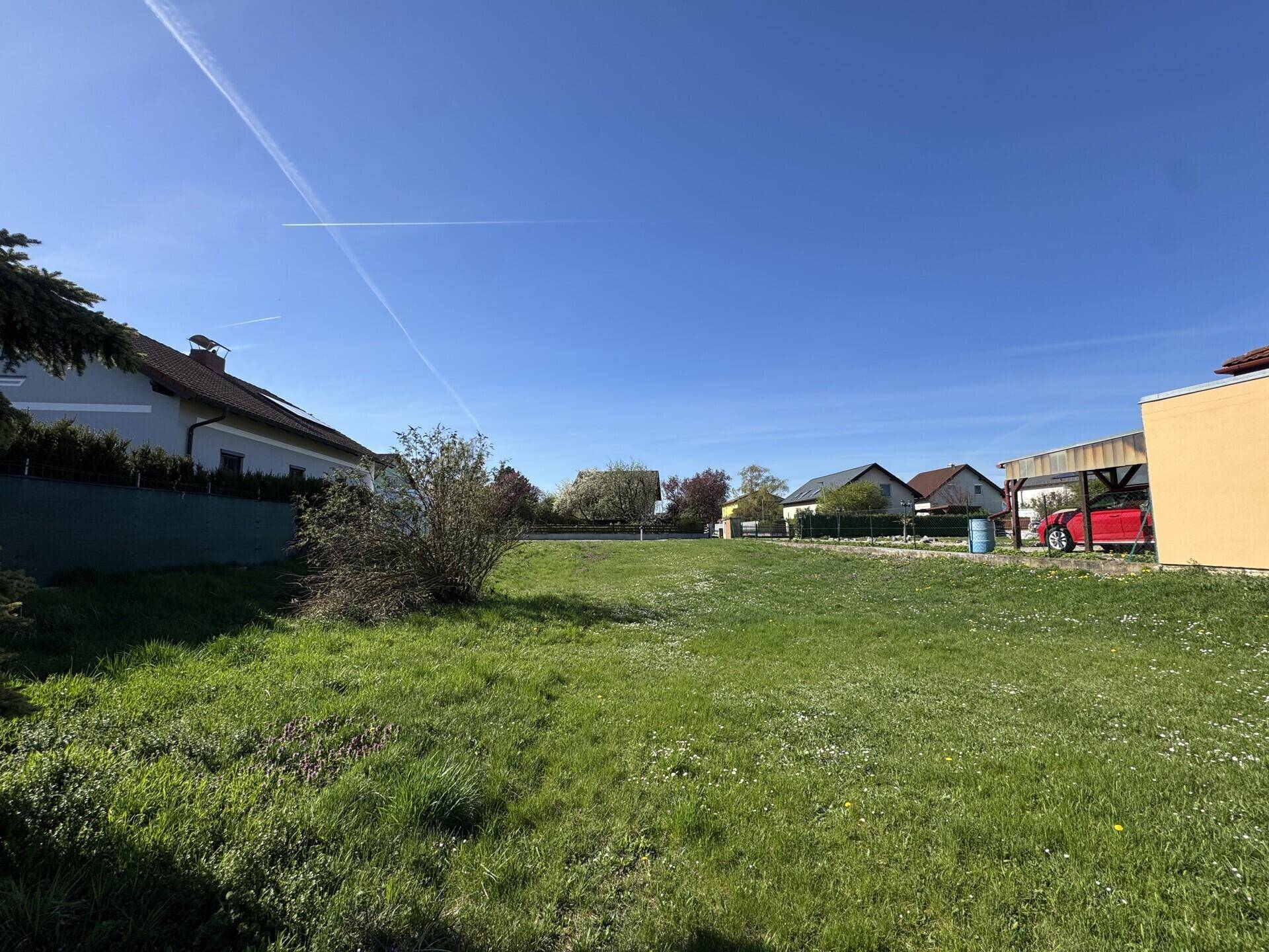 Weitläufiges grünes Grundstück mit Rasenfläche und einem Carport am Rand.
