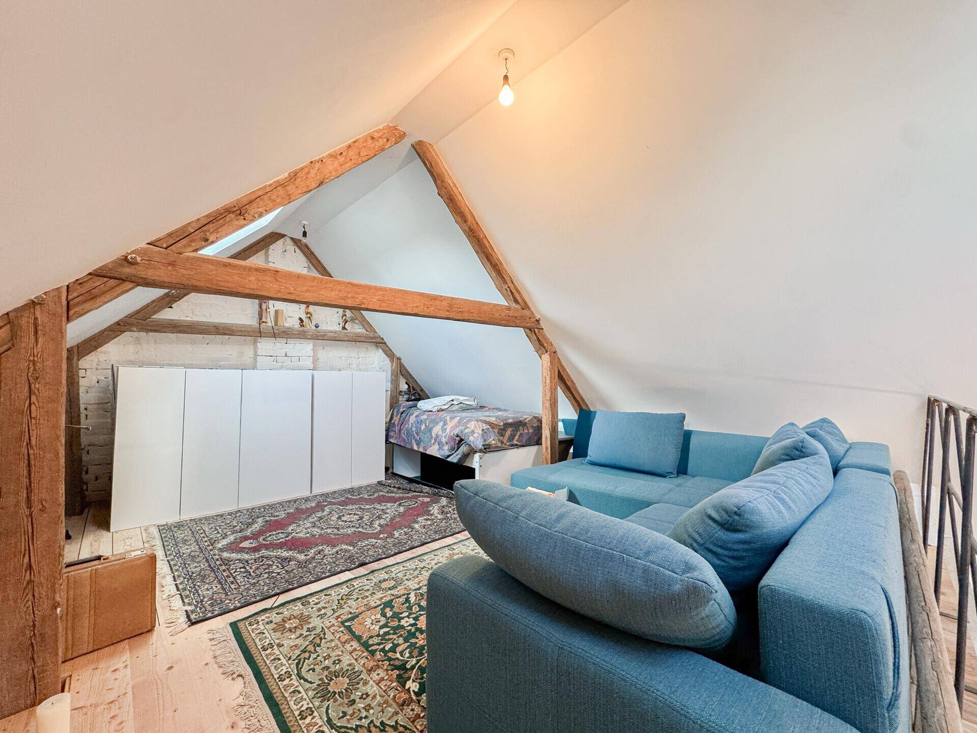 Gemütlicher Schlafbereich im Dachgeschoss mit schrägen Wänden, Holzbalken und Teppichen.