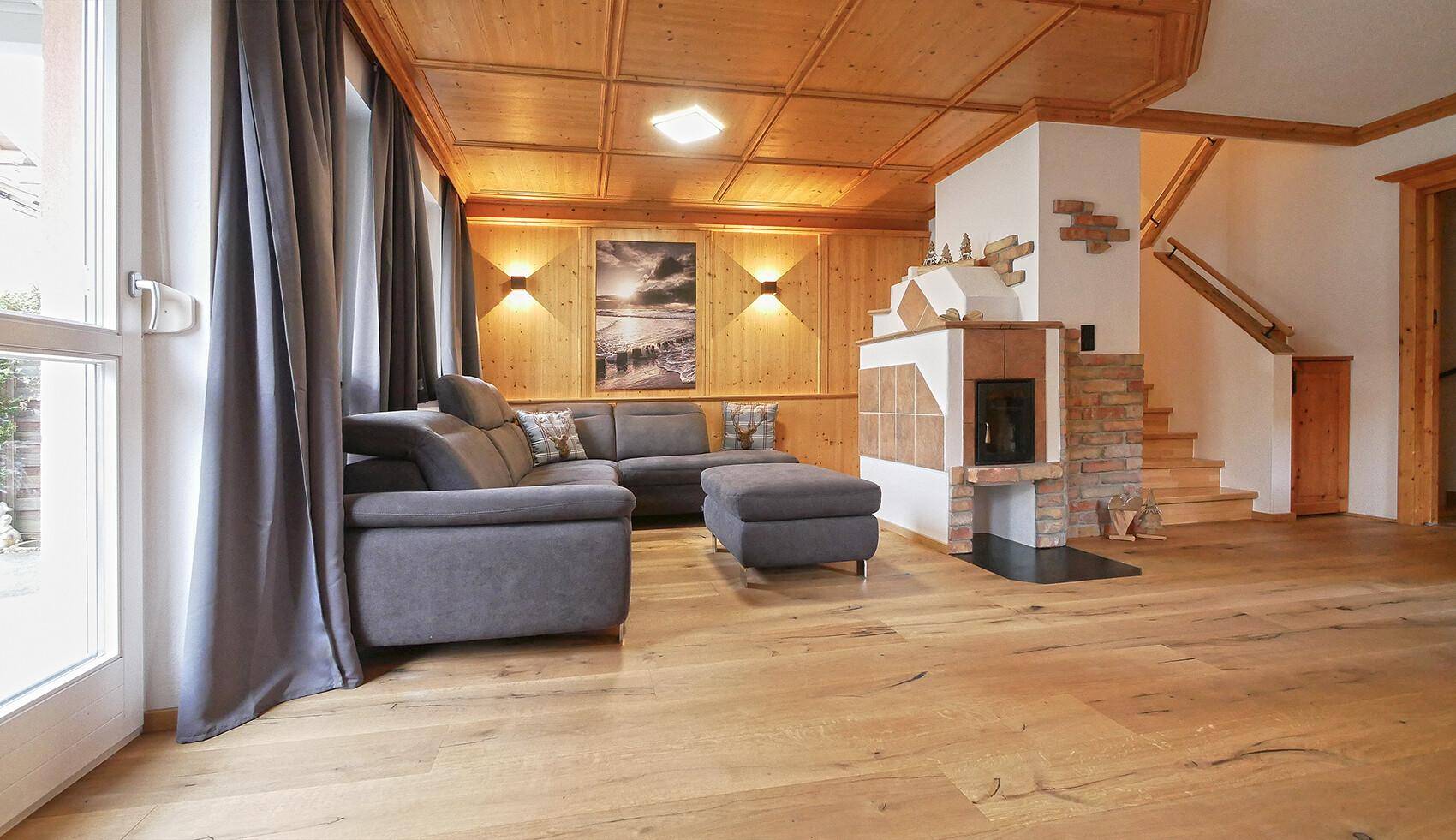 Heller Wohnbereich mit Holzboden, modernem Sofa und traditionellem Kachelofen.