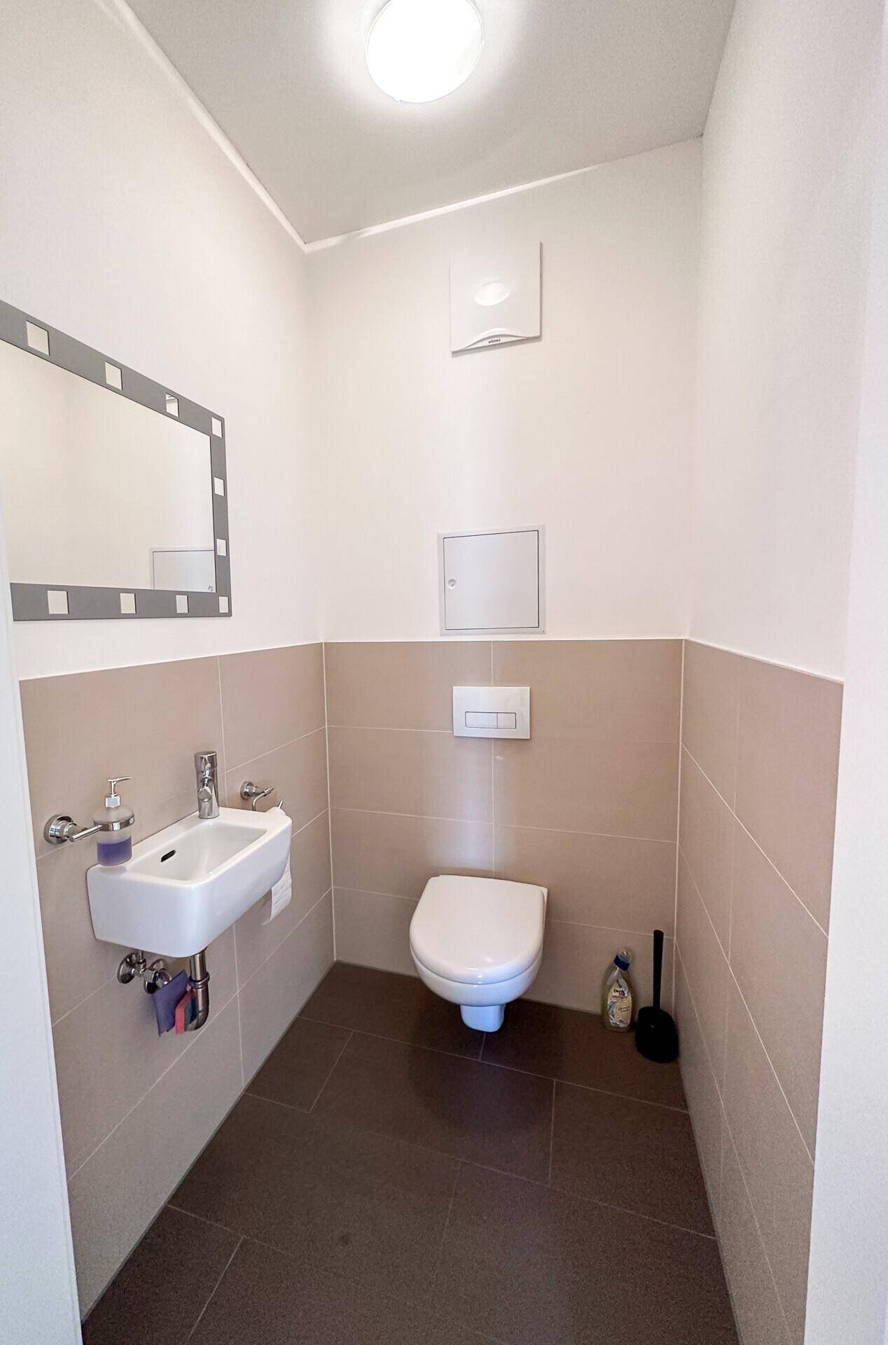 Modernes Gäste-WC mit Wand-WC, kleinem Waschbecken und beigen Fliesen.