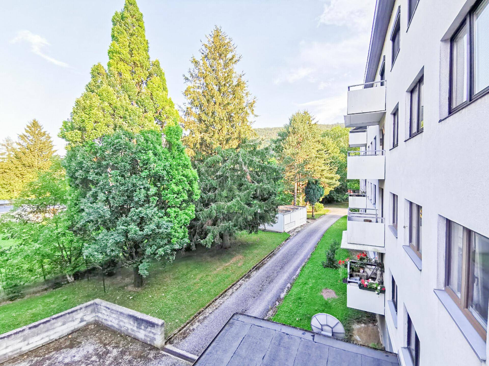 Mehrfamilienhaus mit Balkonen, umgeben von hohen Bäumen und Grünflächen.