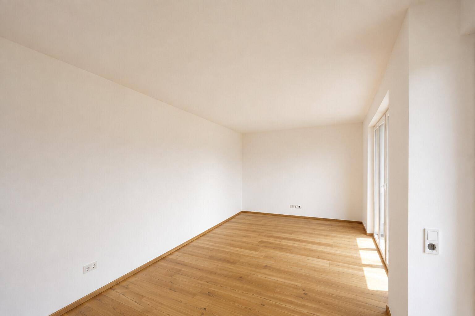 Lichtdurchfluteter Raum mit warmem Holzboden und großen Fenstern, bereit zur individuellen Gestaltung.