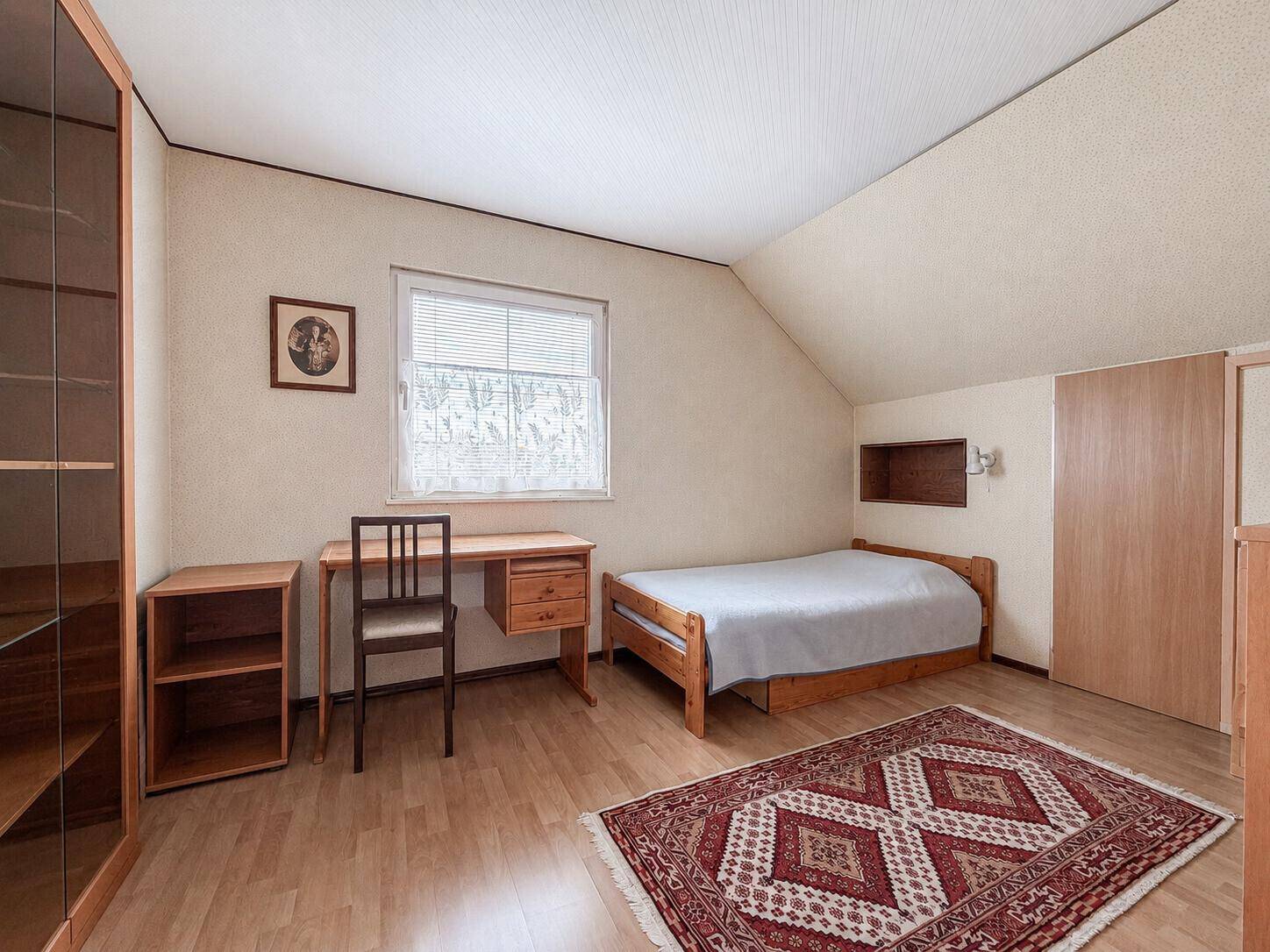Gemütliches Schlafzimmer im Dachgeschoss mit Einzelbett und Holzmöbeln.