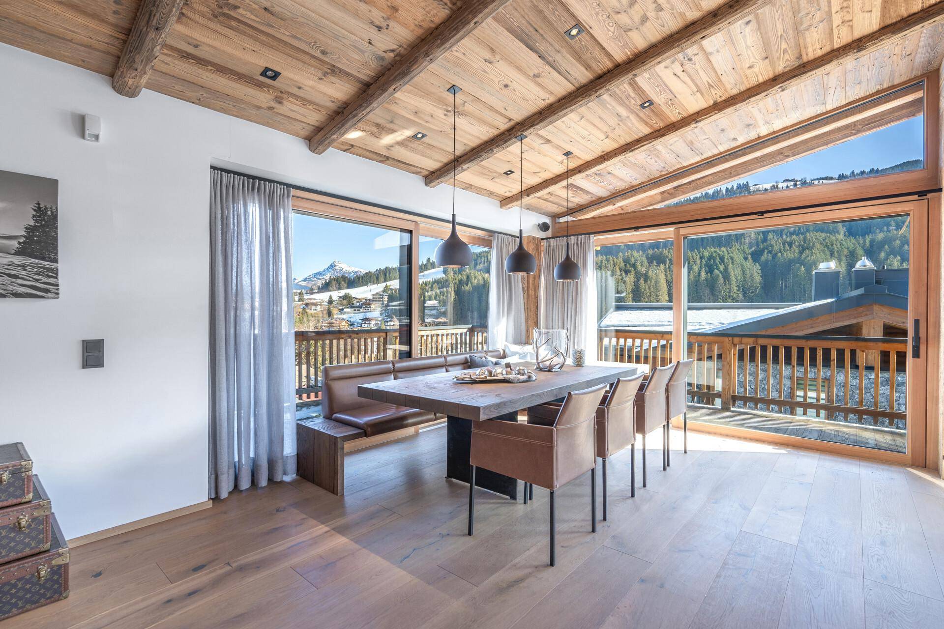 Heller Essbereich mit Holztisch, bequemer Sitzbank und Panoramablick auf die verschneiten Berge.