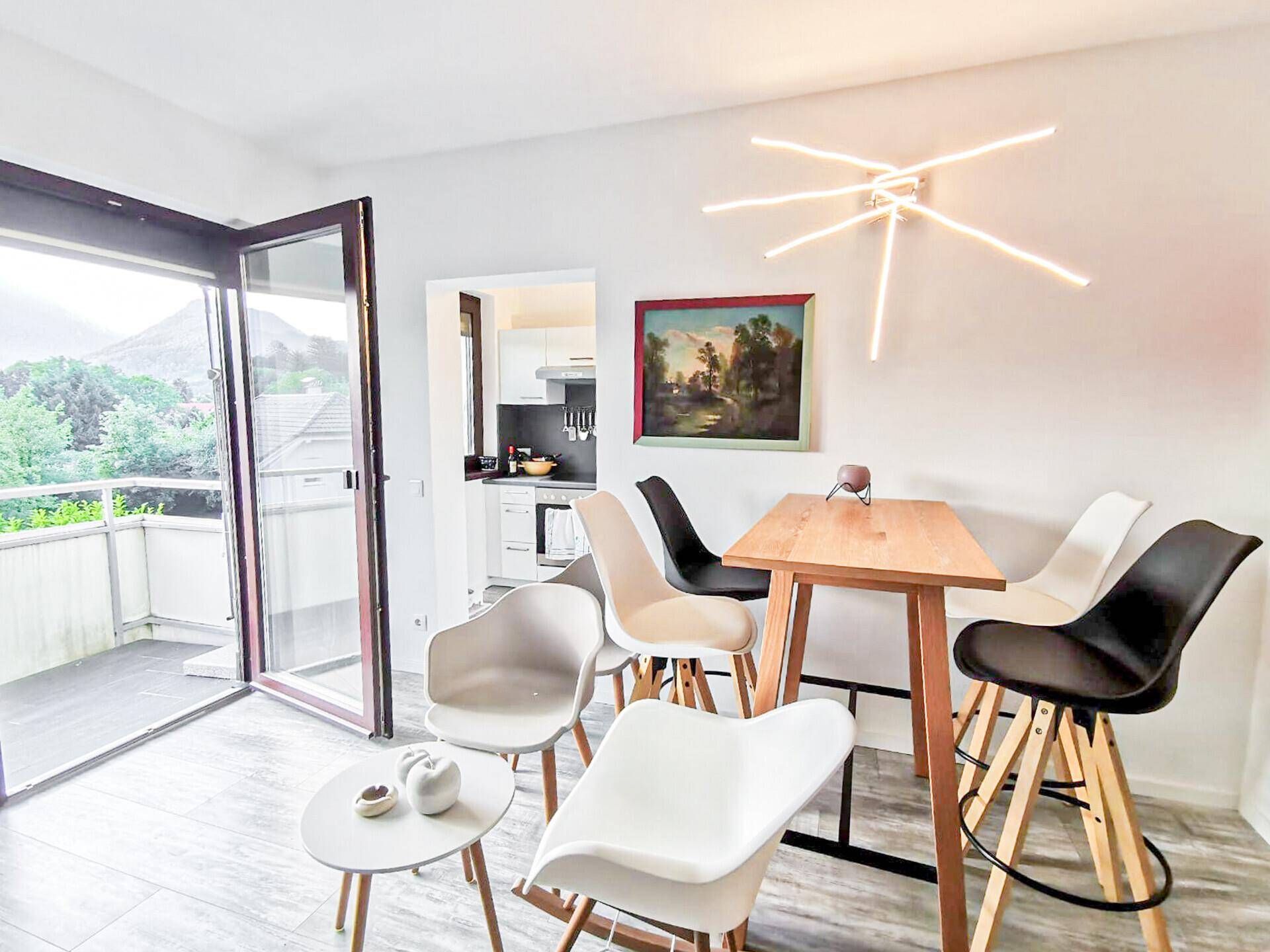 Offener Wohnbereich mit Esstisch, modernen Stühlen und Zugang zu einem Balkon.