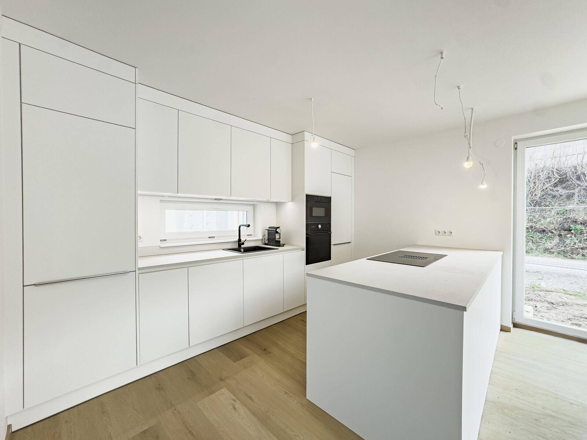 Moderne, weiße Einbauküche mit Kochinsel und integrierten Geräten in neuwertigem Zustand.