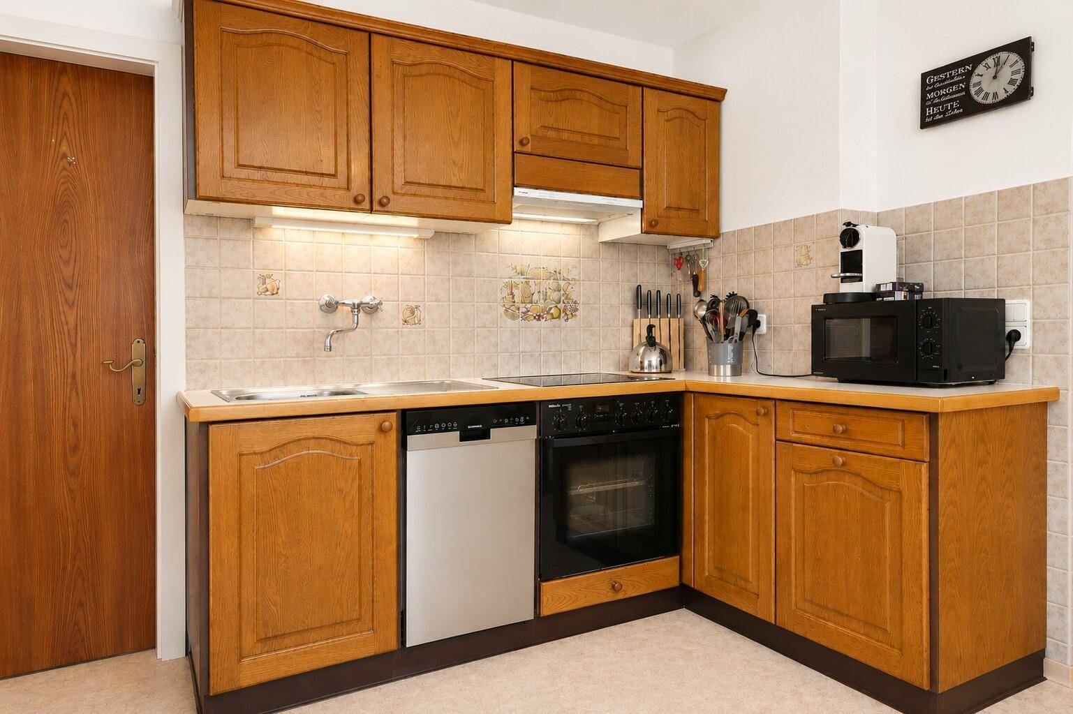 Funktionale Küche im Landhausstil mit Holzschränken, Fliesenrückwand und integrierten Geräten.