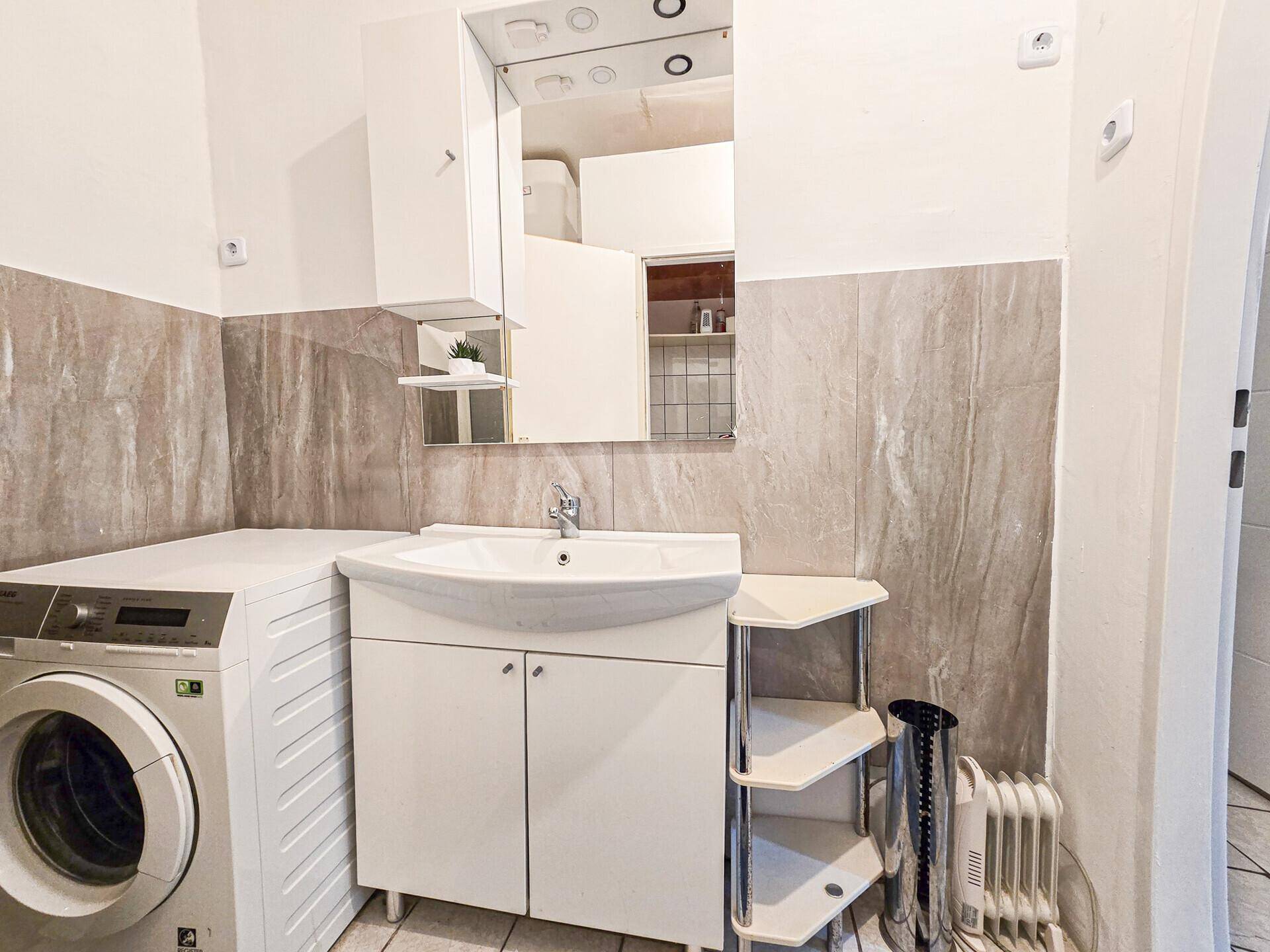 Badezimmer mit Waschbecken, Spiegelschrank, Waschmaschine und Heizlüfter.