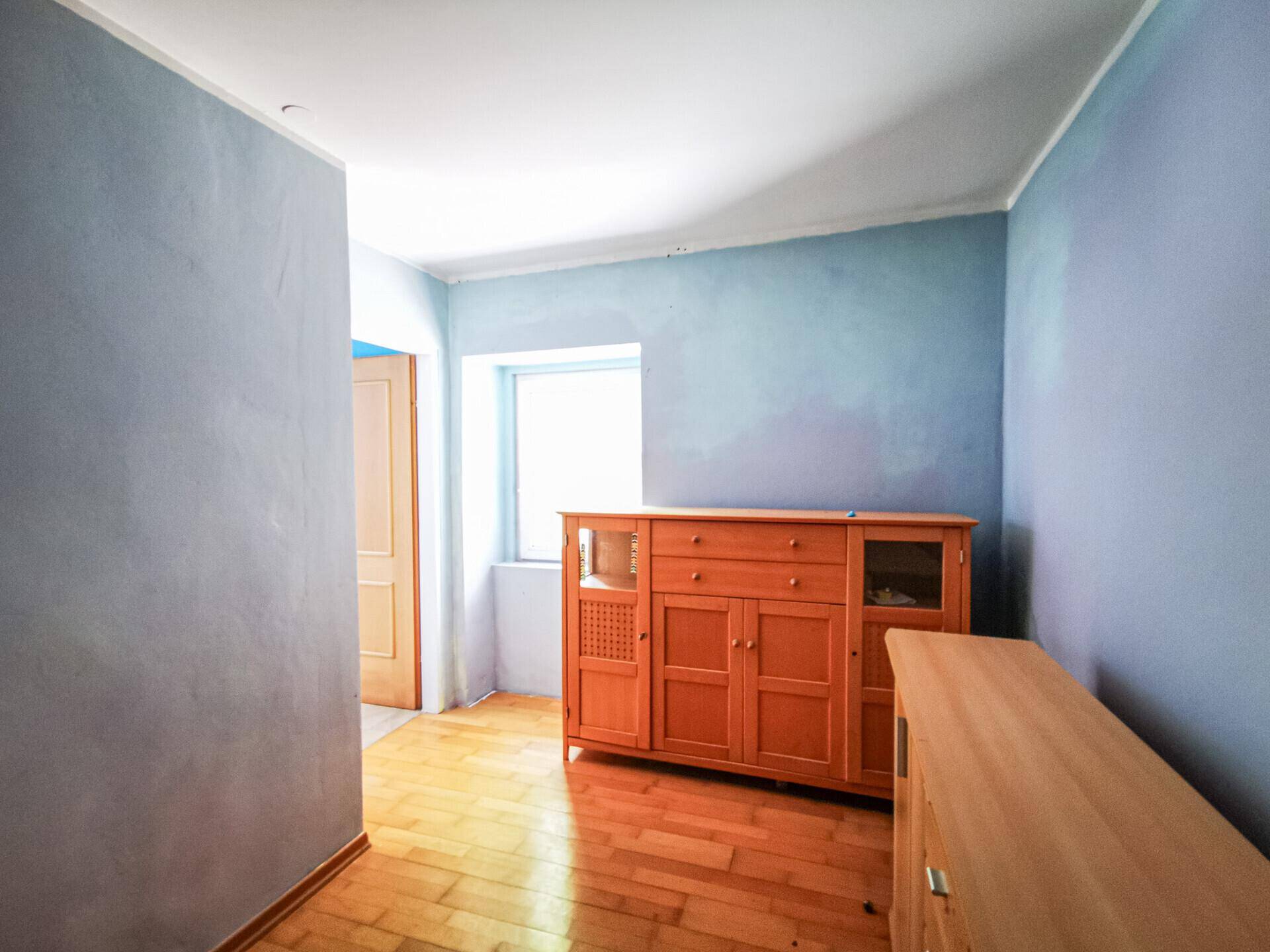Raum mit blauen Wänden, Holzboden, einem Fenster und traditionellen Holzmöbeln.