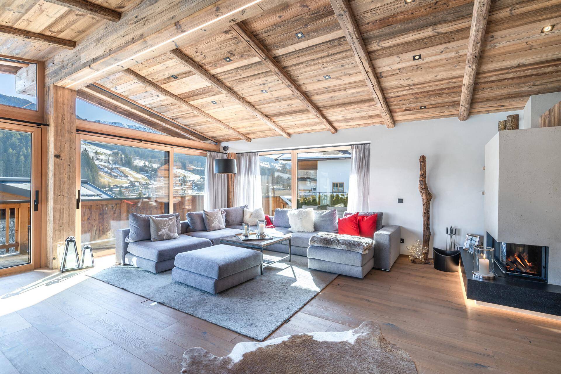 Lichtdurchfluteter Wohnbereich mit modernem Kamin, bequemen Sofas und Blick auf die Berglandschaft.